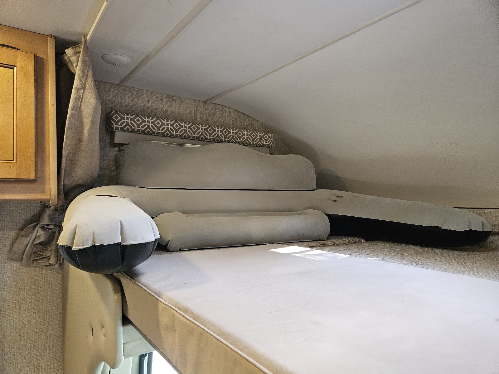 Overhead bunk in an RV rental, featuring a white mattress, inflatable cushions, and a patterned headboard. Cozy sleeping space.. Thor Freedom Elite 2017