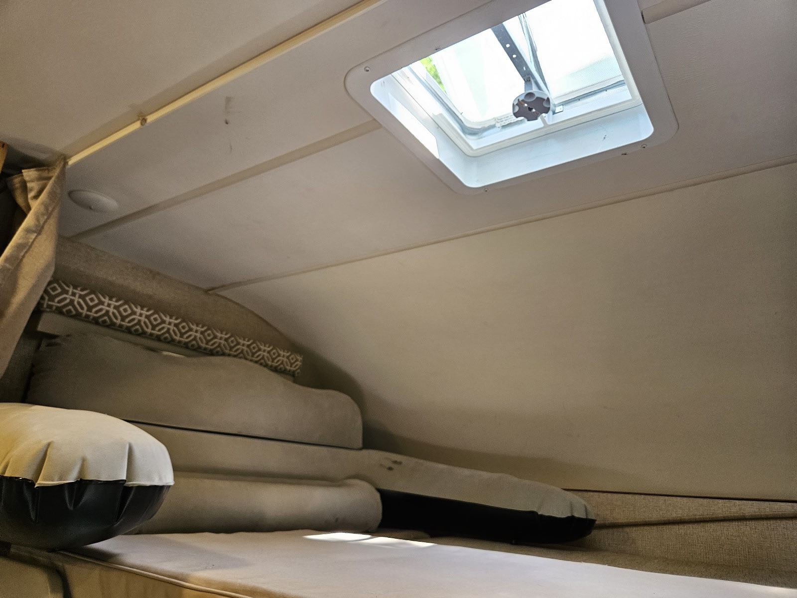 RV rental bunk interior with an open skylight, revealing stacked cushions and an inflatable pillow for comfort.. Thor Freedom Elite 2017