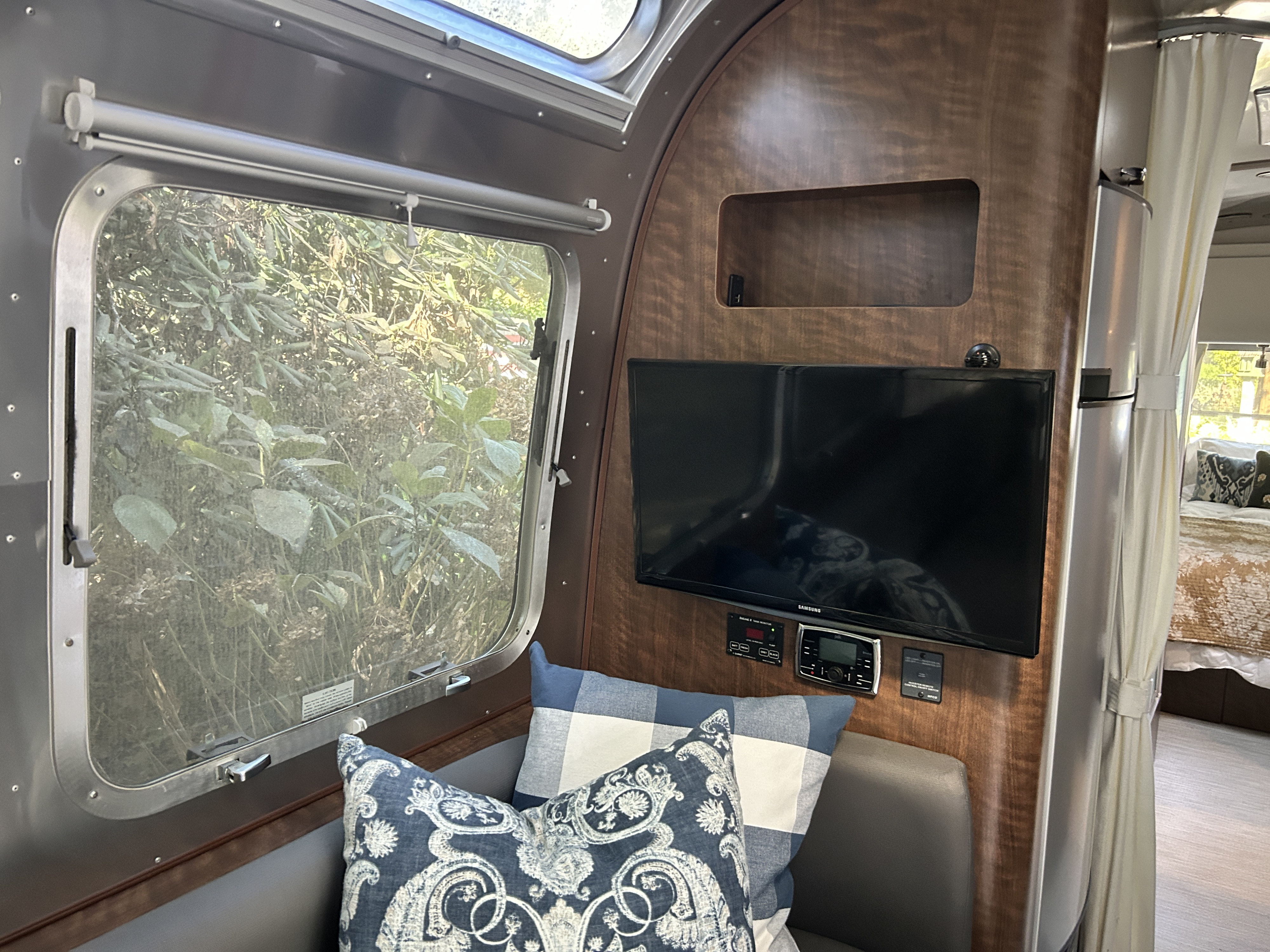 Inside an RV rental: large window with nature view, TV mounted on wood paneling, and decorative cushions for comfort.. Airstream Globetrotter 2018