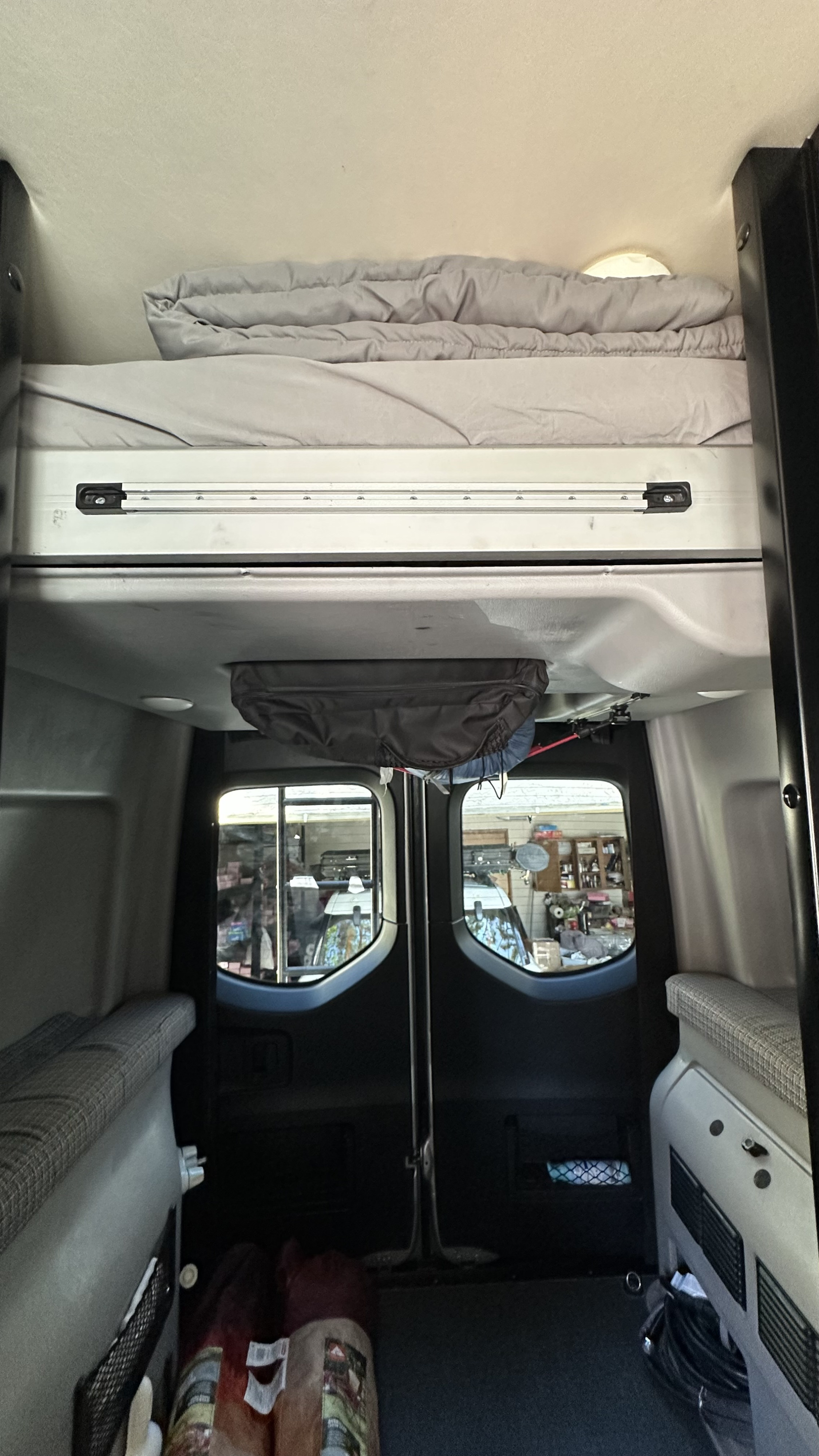 View inside an rv rental, featuring an overhead bunk bed, hanging storage, and rear doors with windows.. Winnebago Revel 2021