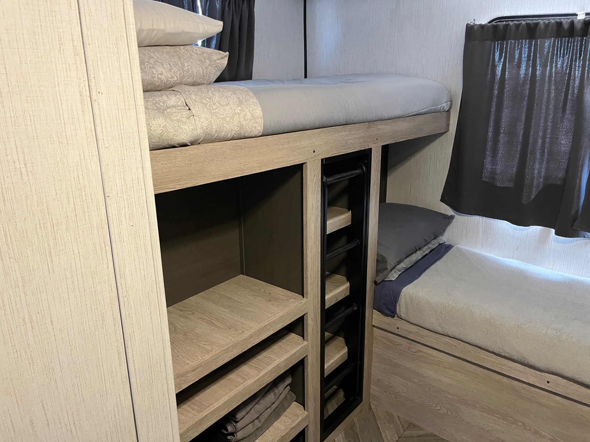 Cozy RV rental bunk beds with a ladder, storage shelves, and gray bedding in a light wood interior.. Heartland RVs Prowler 2022