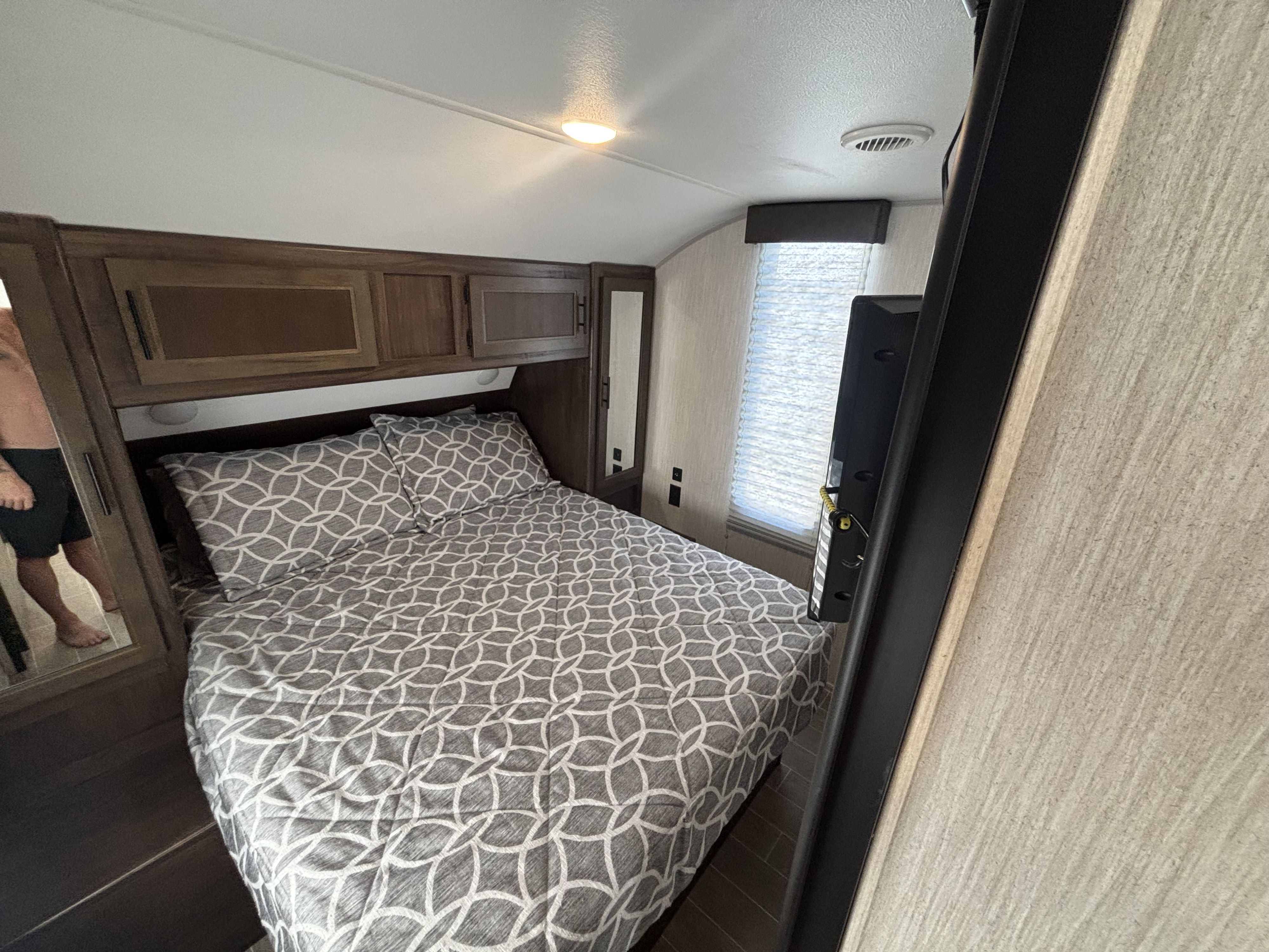 Cozy RV rental bedroom featuring a bed with patterned bedding, wooden overhead cabinets, and a mounted TV.. Forest River Cherokee Grey Wolf 2020