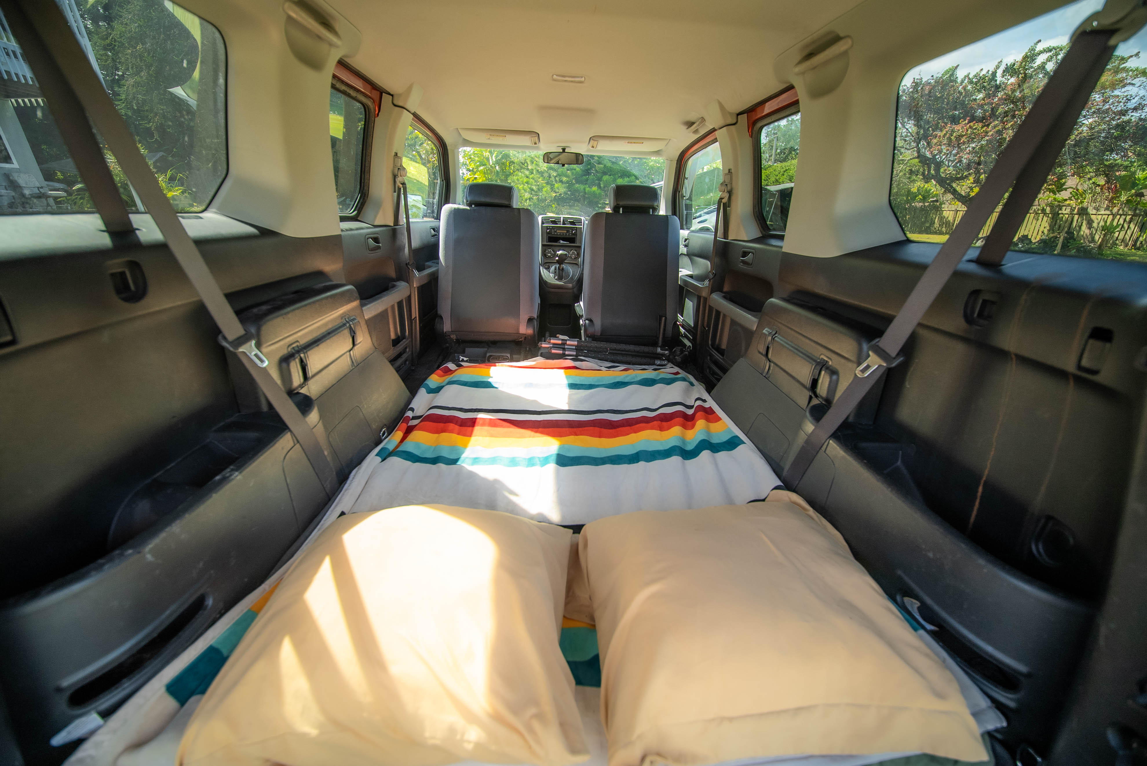Cozy car camping setup inside an RV rental, featuring a striped blanket and pillows in the vehicle's rear, ready for adventure.. Honda Element 2004