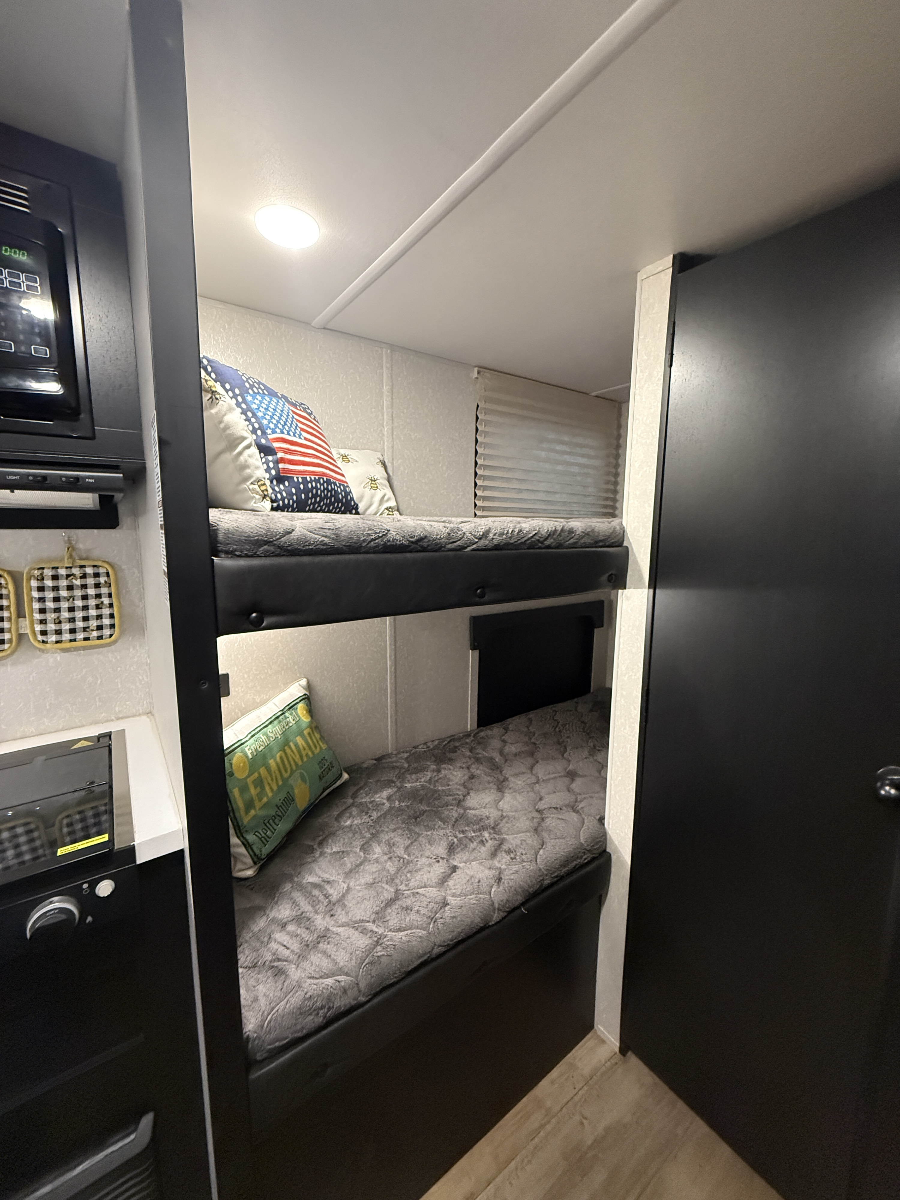 Cozy bunk beds in an rv rental, featuring patriotic & lemonade pillows, with a microwave & kitchen counter nearby.. Forest River Cherokee Wolf Pup Black Label 2021