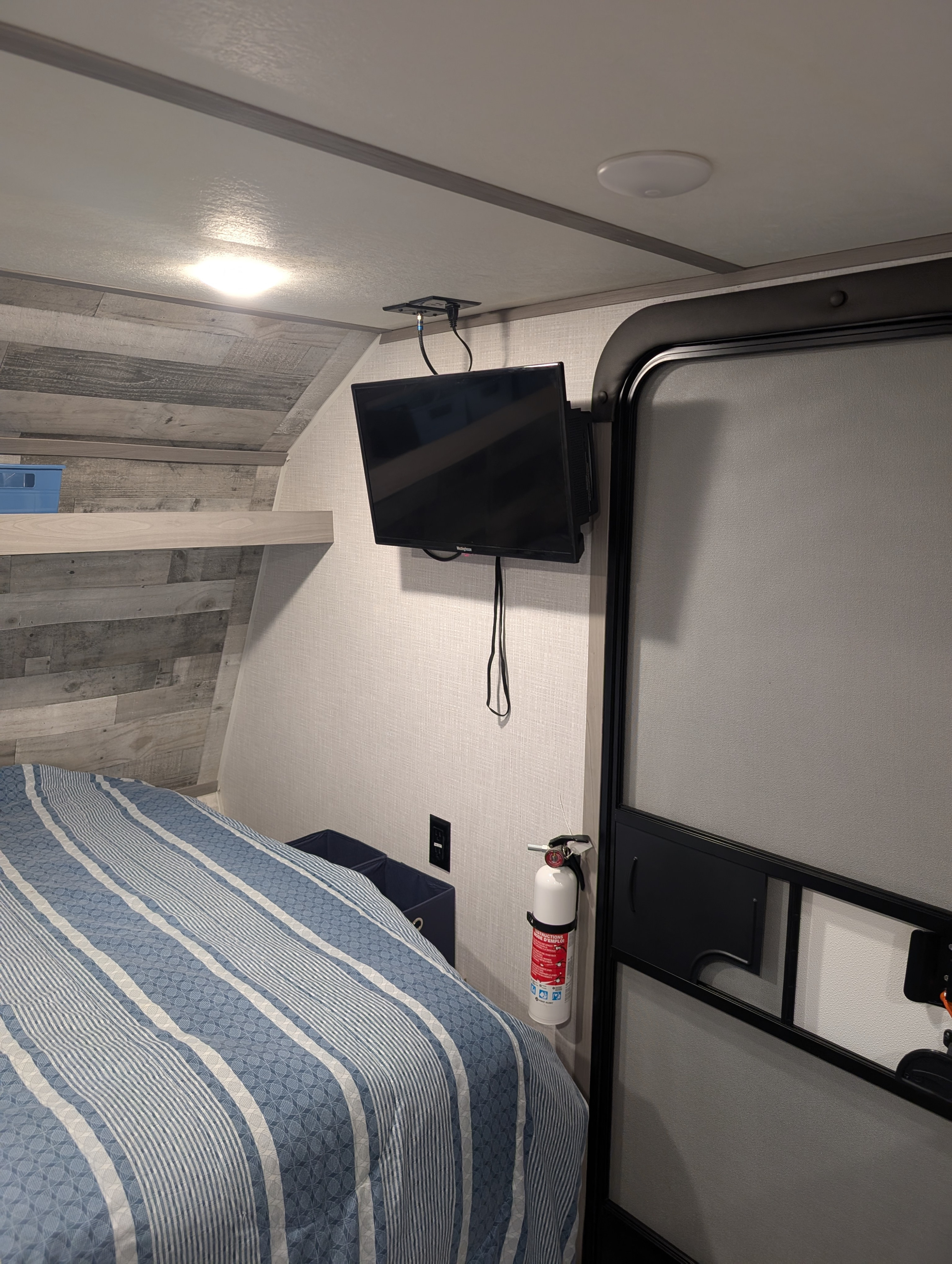 Cozy RV rental bedroom featuring a wall-mounted TV, comfortable striped bed, and a visible fire extinguisher for safety.. Dutchmen Coleman Lantern LT 2023
