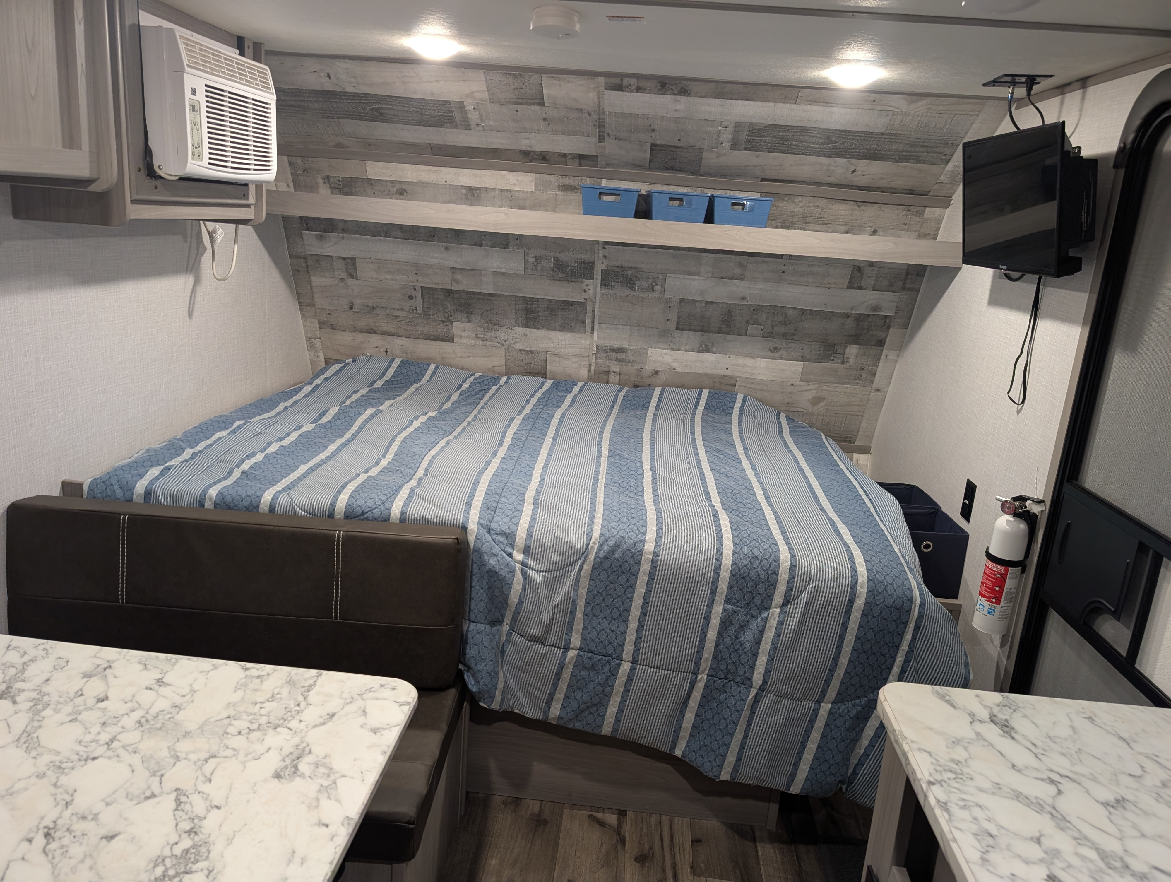 Cozy RV rental bedroom/dinette space: striped bed, marble tables, AC, TV, wood-panel wall, and built-in storage.. Dutchmen Coleman Lantern LT 2023