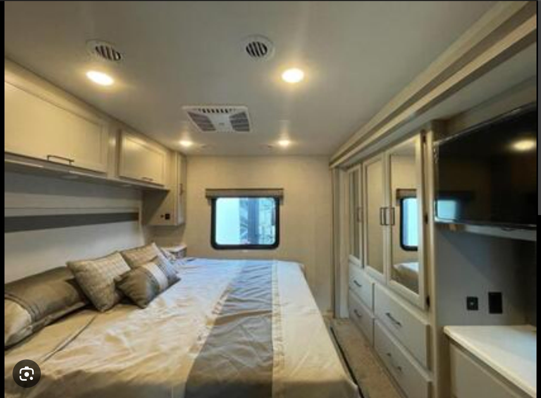 Spacious RV rental bedroom featuring a large bed, overhead storage, mirrored wardrobe, and TV, offering comfort on the road.. Thor Windsport 2023