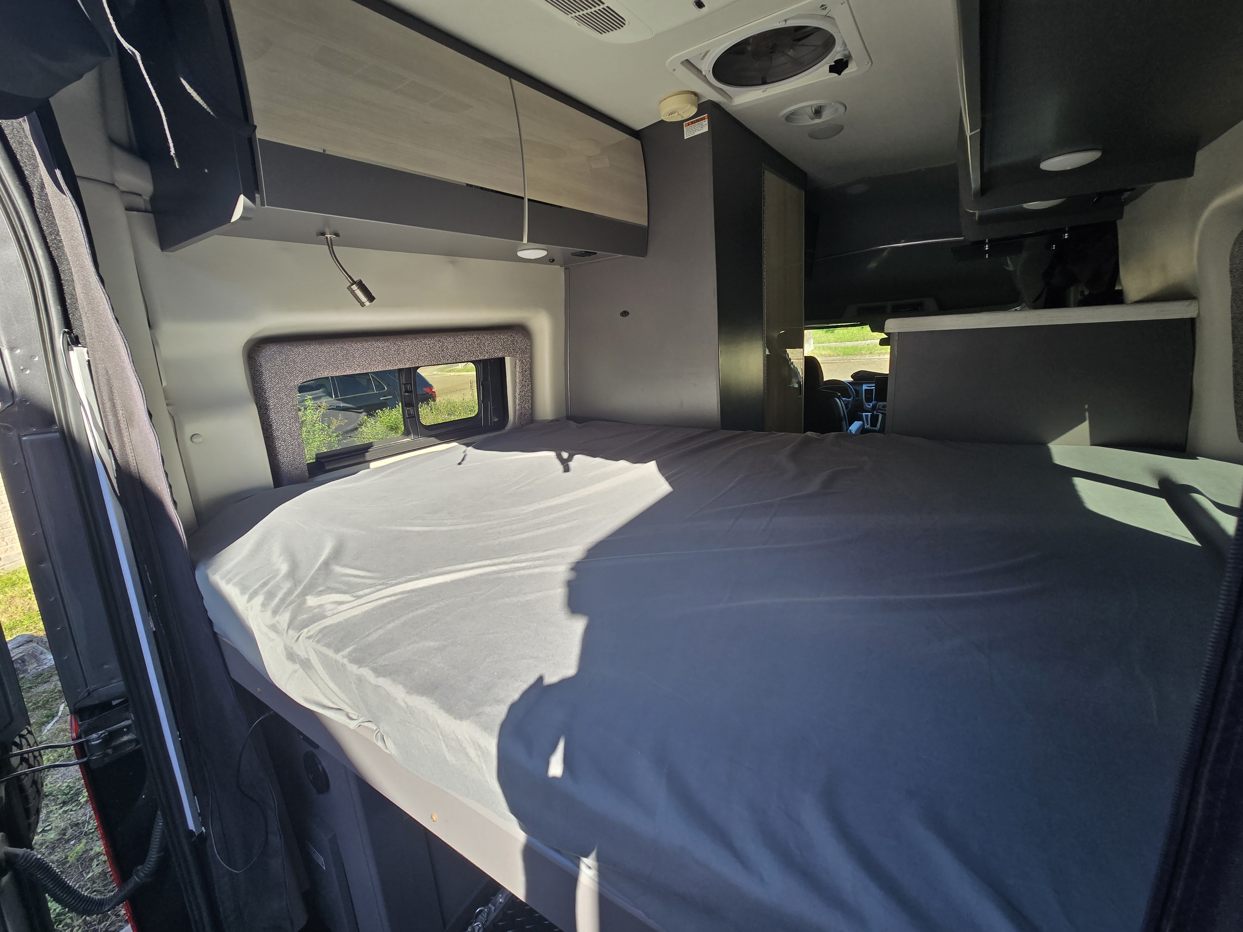 Interior of an RV rental showing a large bed, overhead cabinets, and a window with outside views for comfortable travel.. Thor Motor Coach Tranquility 19LT 2023