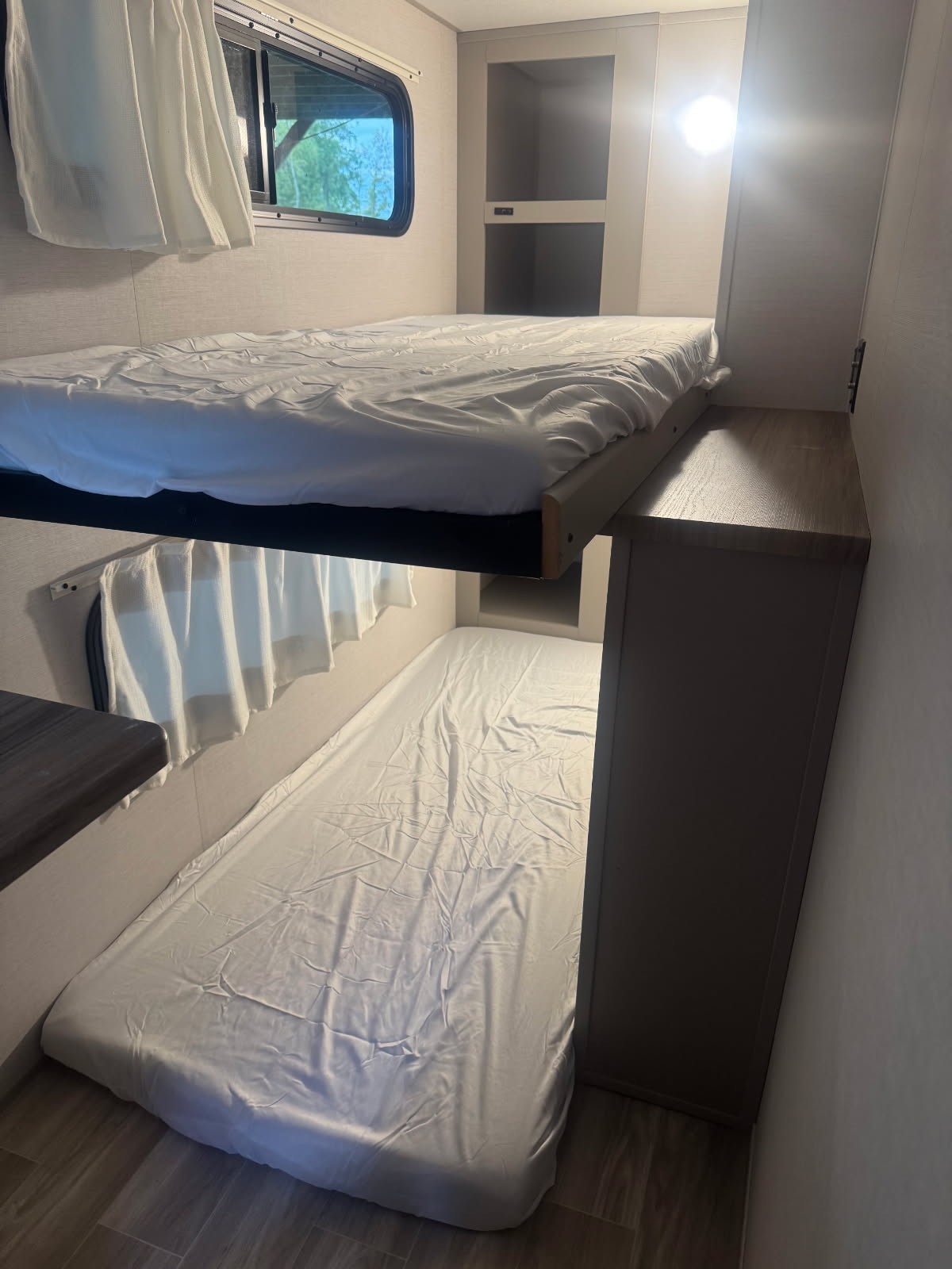 Inside an RV rental: two stacked bunk beds with white sheets, a window revealing trees, and built-in storage.. Forest River Vibe 2024