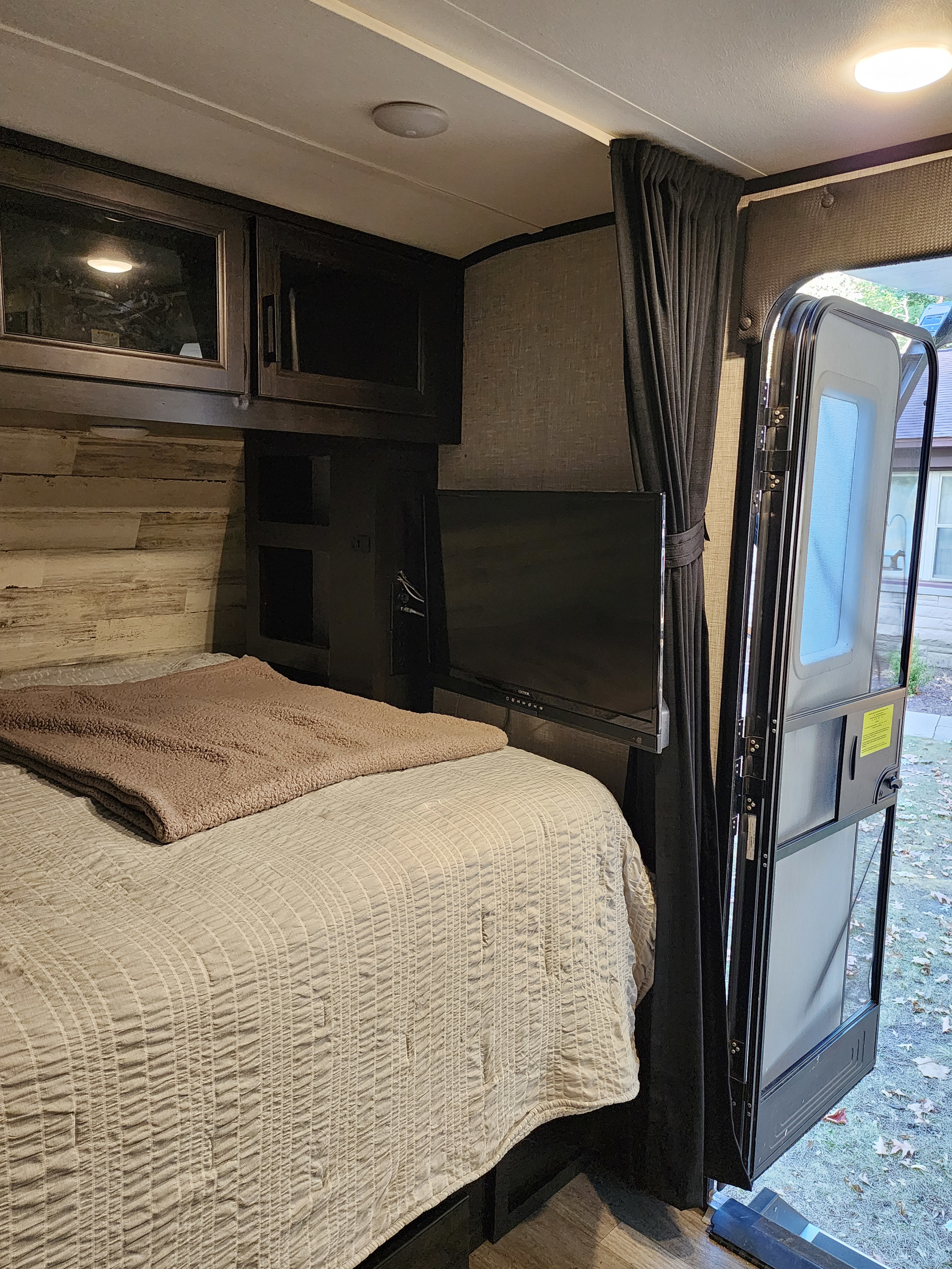 Cozy RV rental bedroom with a comfy bed, TV, dark cabinets, and an open door revealing the outdoors. Perfect for travel!. Jayco Jay Feather Micro 2022
