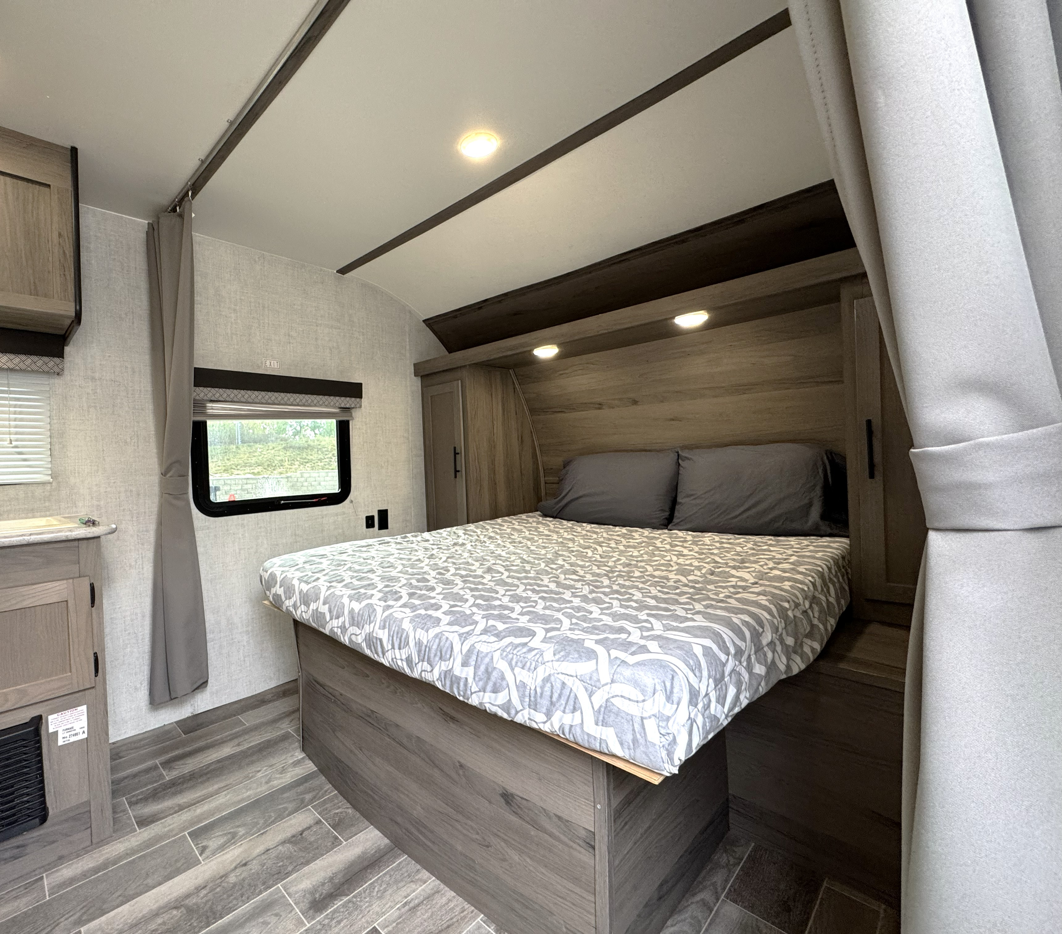 Explore this cozy RV rental bedroom featuring a large bed with grey pillows, wood-look cabinets, and bright overhead lighting.. Gulf Stream Amerilite 2021