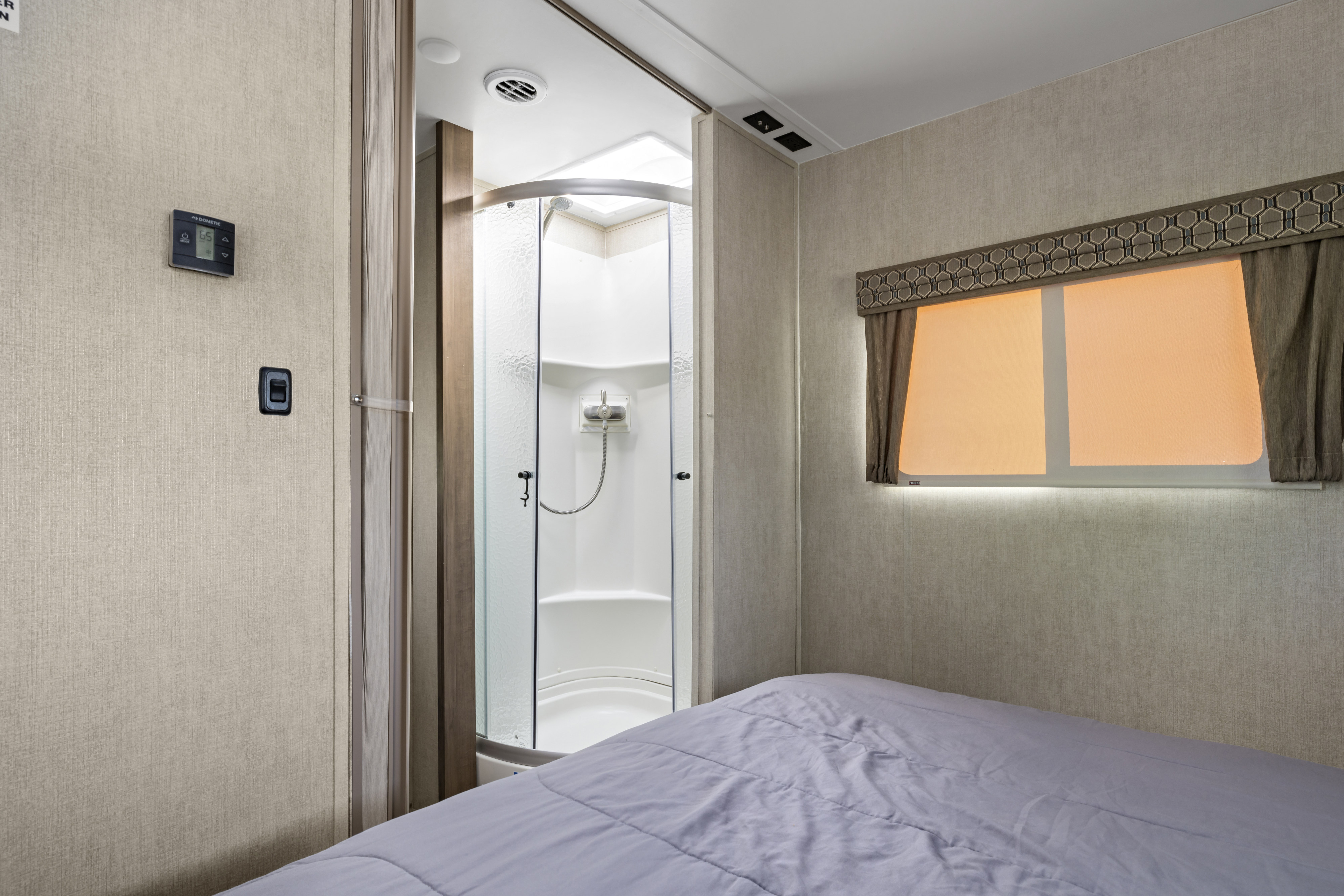 RV rental: Compact interior with a bed, corner shower, window with blinds, and a Dometic thermostat set to 65 degrees.. Gulf Stream Conquest 2021