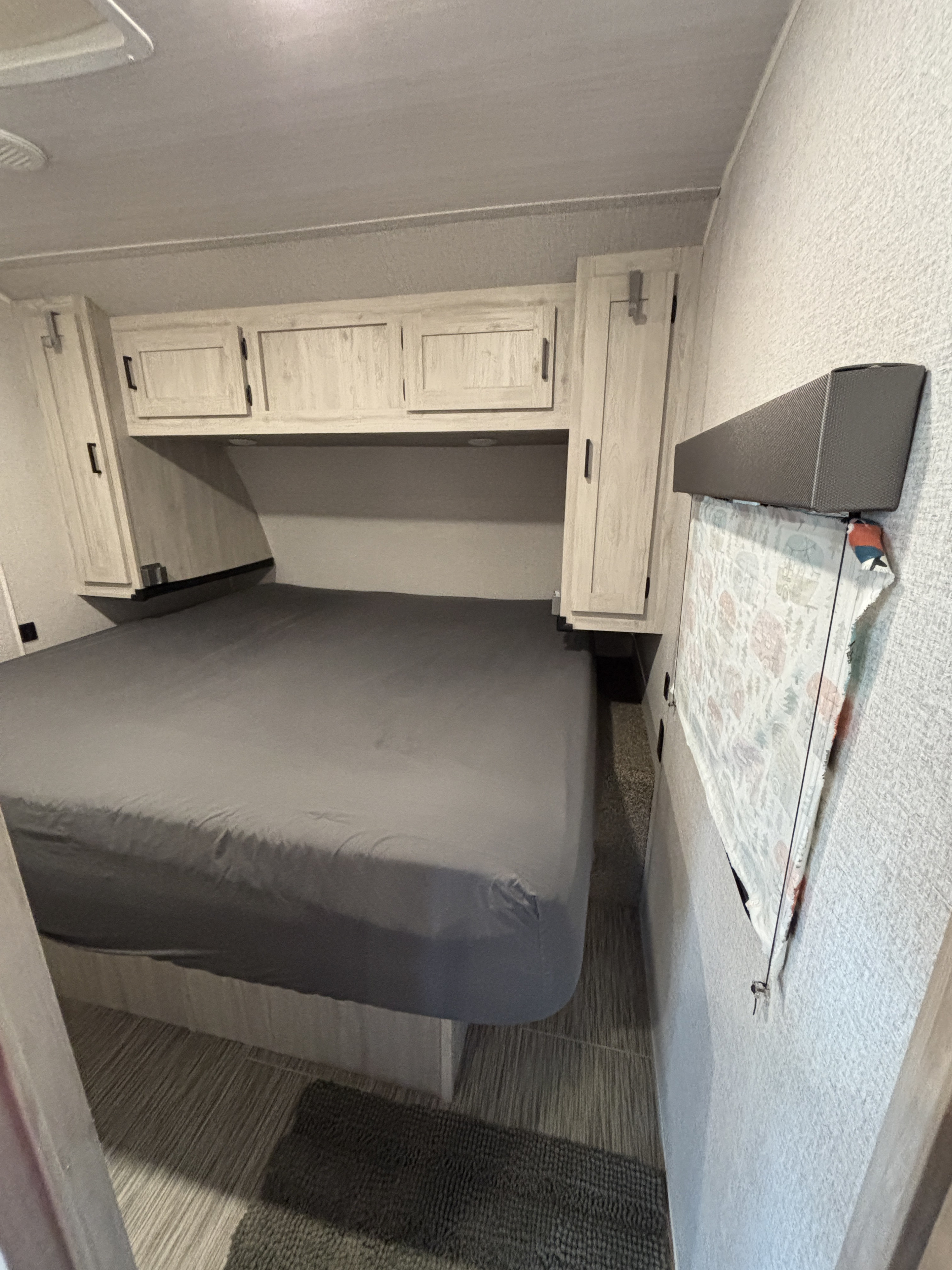 RV rental bedroom featuring a gray bed, ample overhead and side storage cabinets, and clean, functional decor.. East to West Silver Lake 27K2D 2023