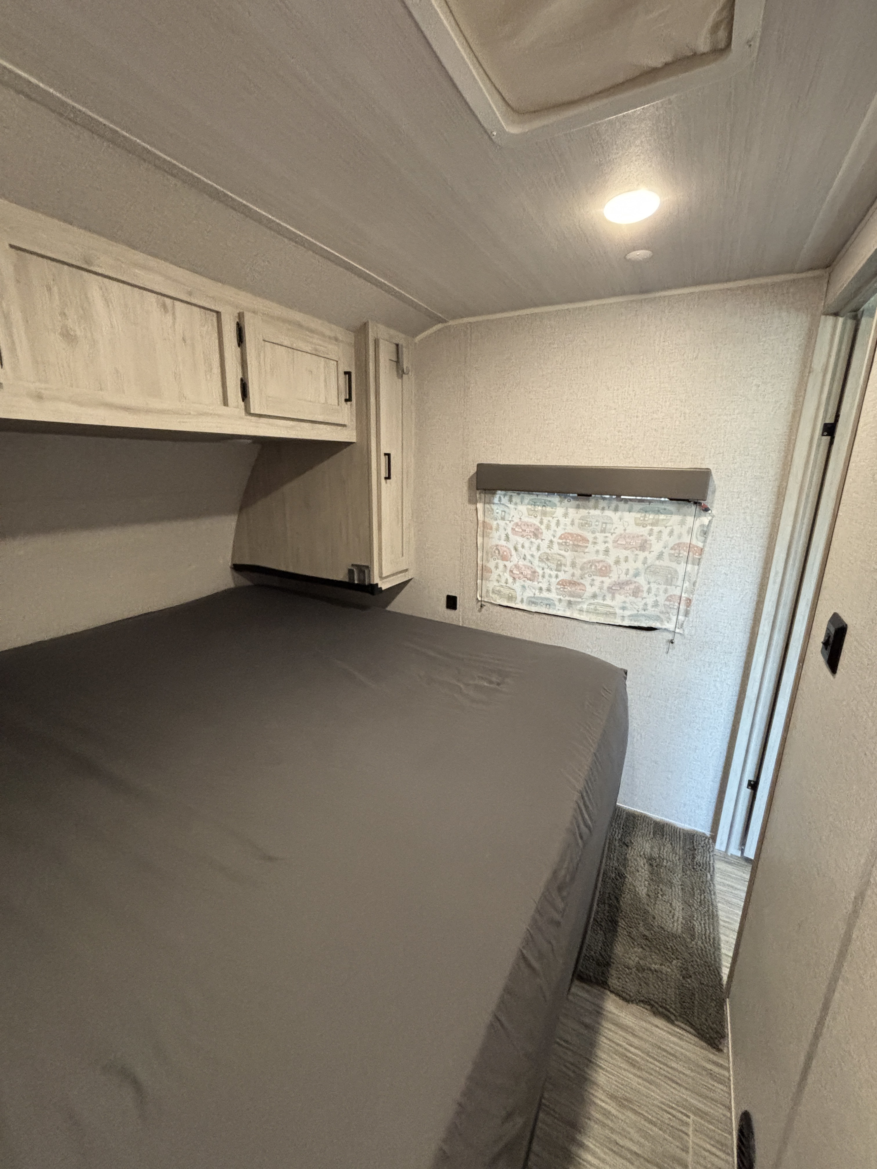 Experience comfort in this RV rental bedroom with overhead storage, a wide bed, and a delightful camper-patterned window.. East to West Silver Lake 27K2D 2023