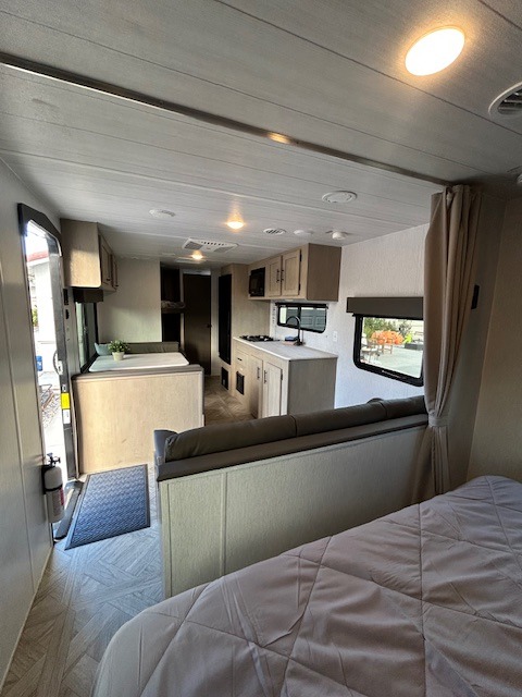 This bright, modern RV rental interior features a spacious kitchen, living area, and a cozy bedroom in the foreground.. Forest River Salem Cruise Lite 2024