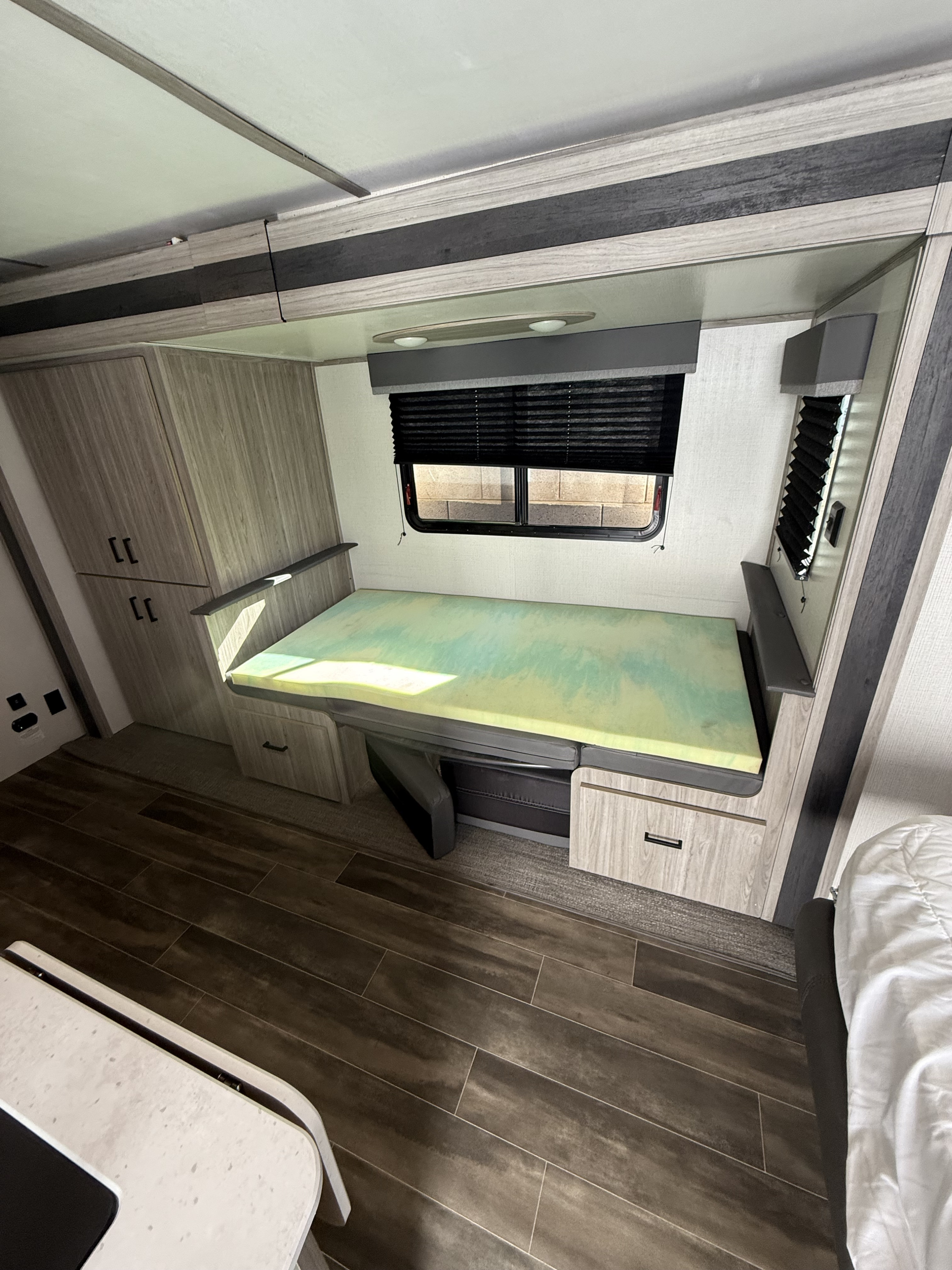 RV rental interior showing a convertible bed with a foam topper, storage cabinets, and a window with blinds.. Keystone RV Passport SL 2022