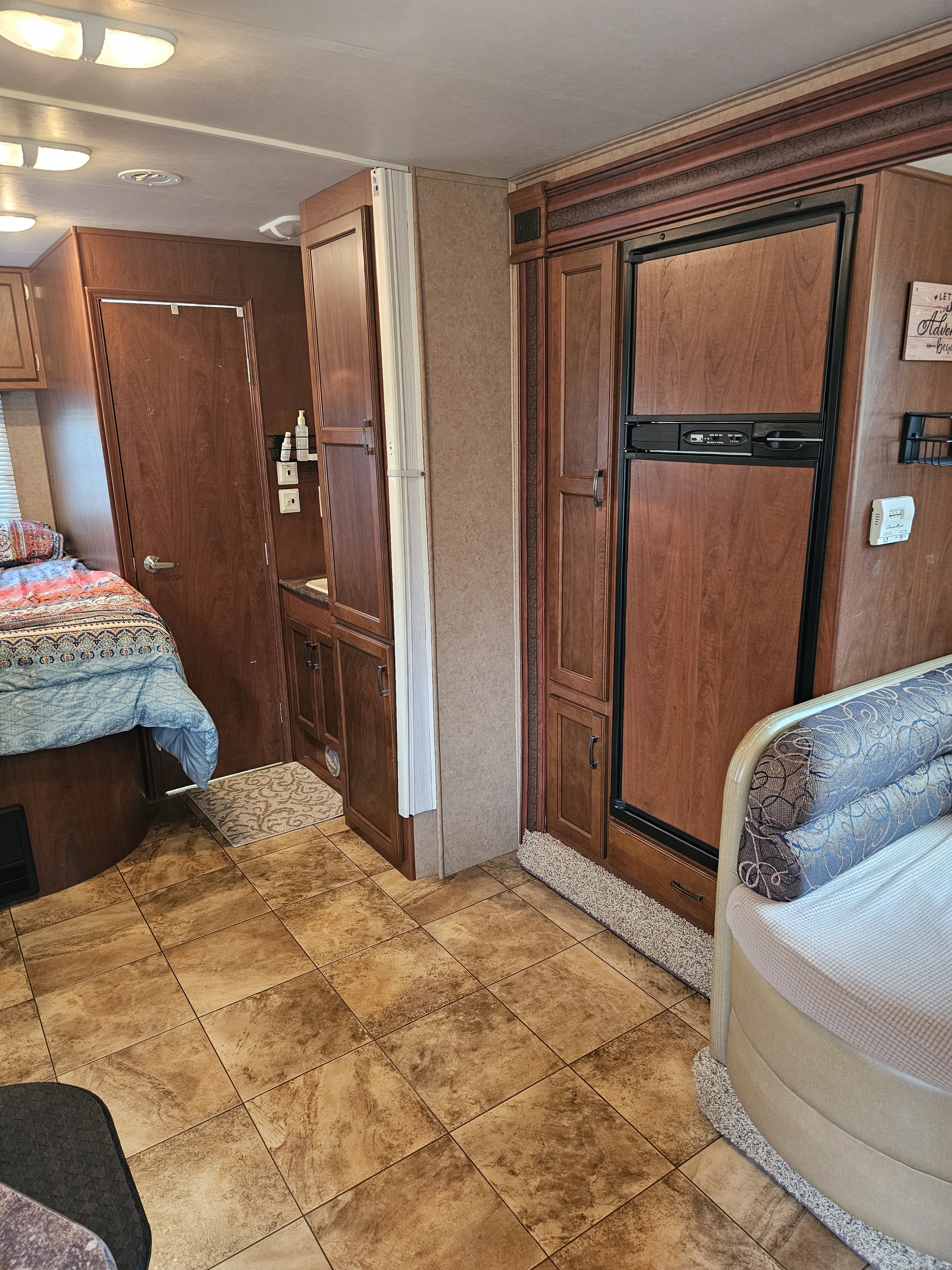 Cozy RV rental interior with a bedroom, compact kitchen/fridge, wood cabinets, and tiled floor, ideal for comfortable travel.. Jayco Redhawk 2013