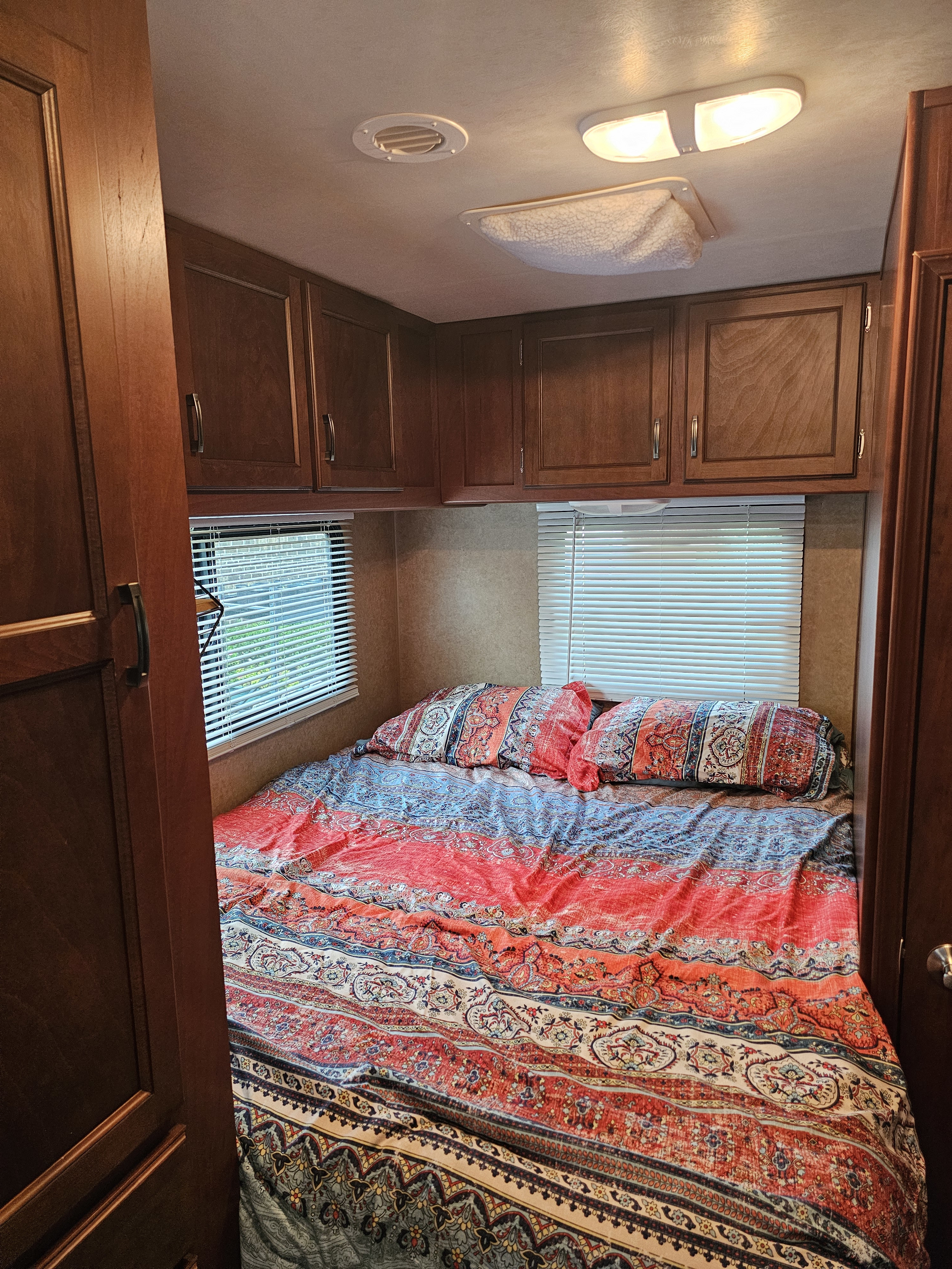 Cozy RV rental bedroom featuring a patterned bed, overhead cabinets, and windows with blinds.. Jayco Redhawk 2013