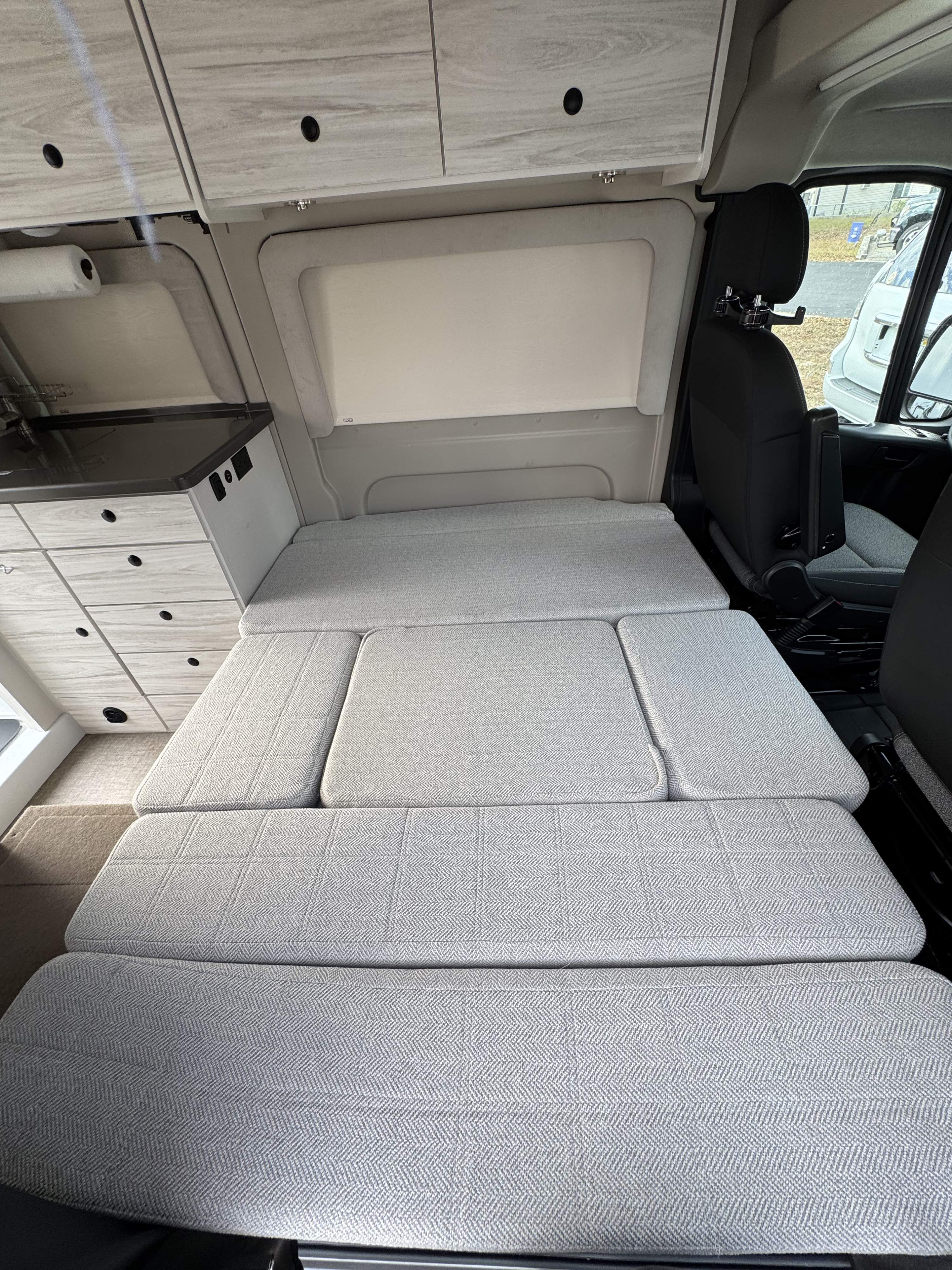 Spacious RV rental interior with a cozy grey bed/seating, kitchen counter, and overhead cabinets for storage.. Entegra ARC 18C 2025