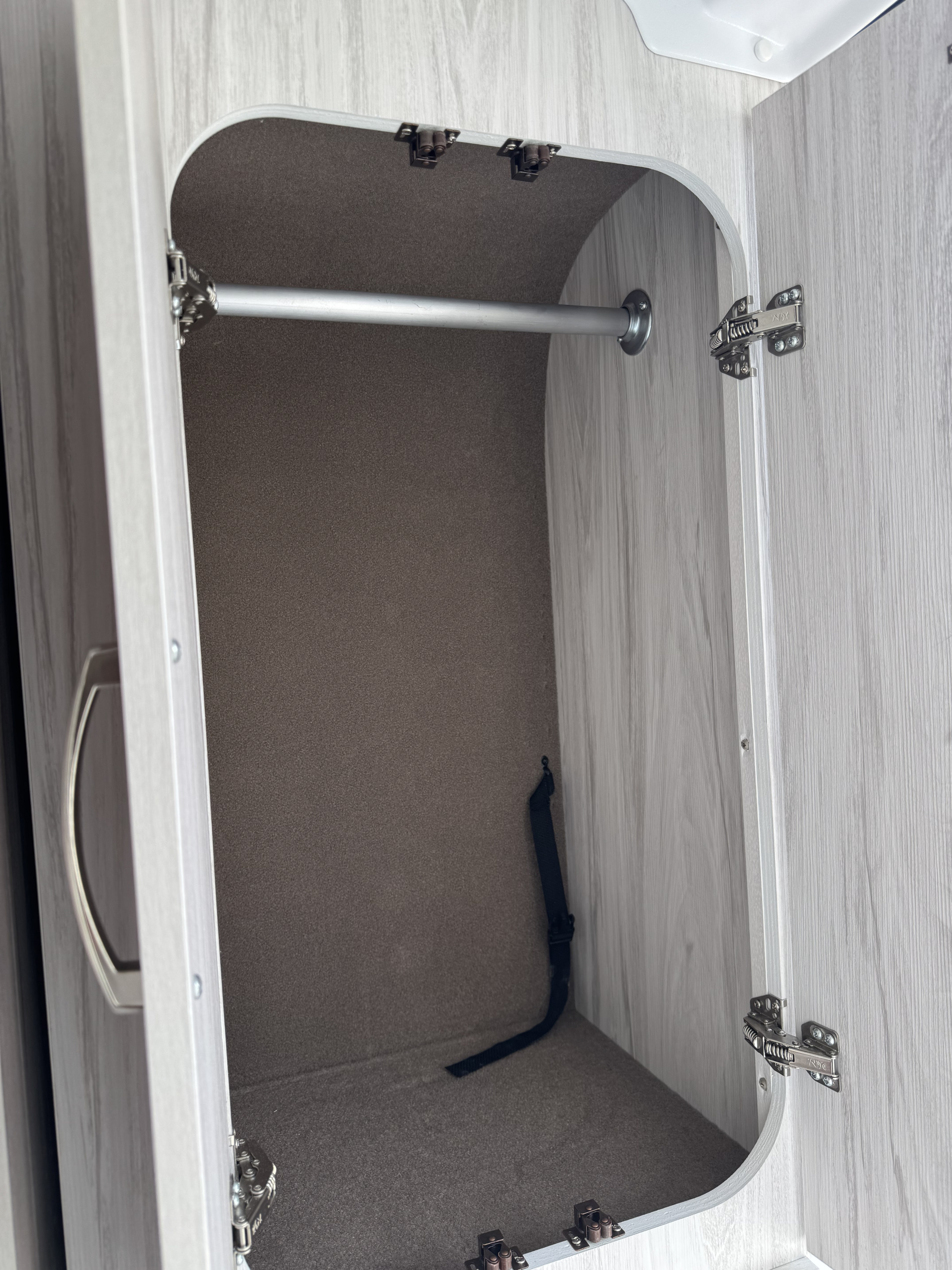 Inside an RV rental, this compact wardrobe features a clothes hanging rod, soft carpeted interior, and a securing strap.. Entegra ARC 18C 2025