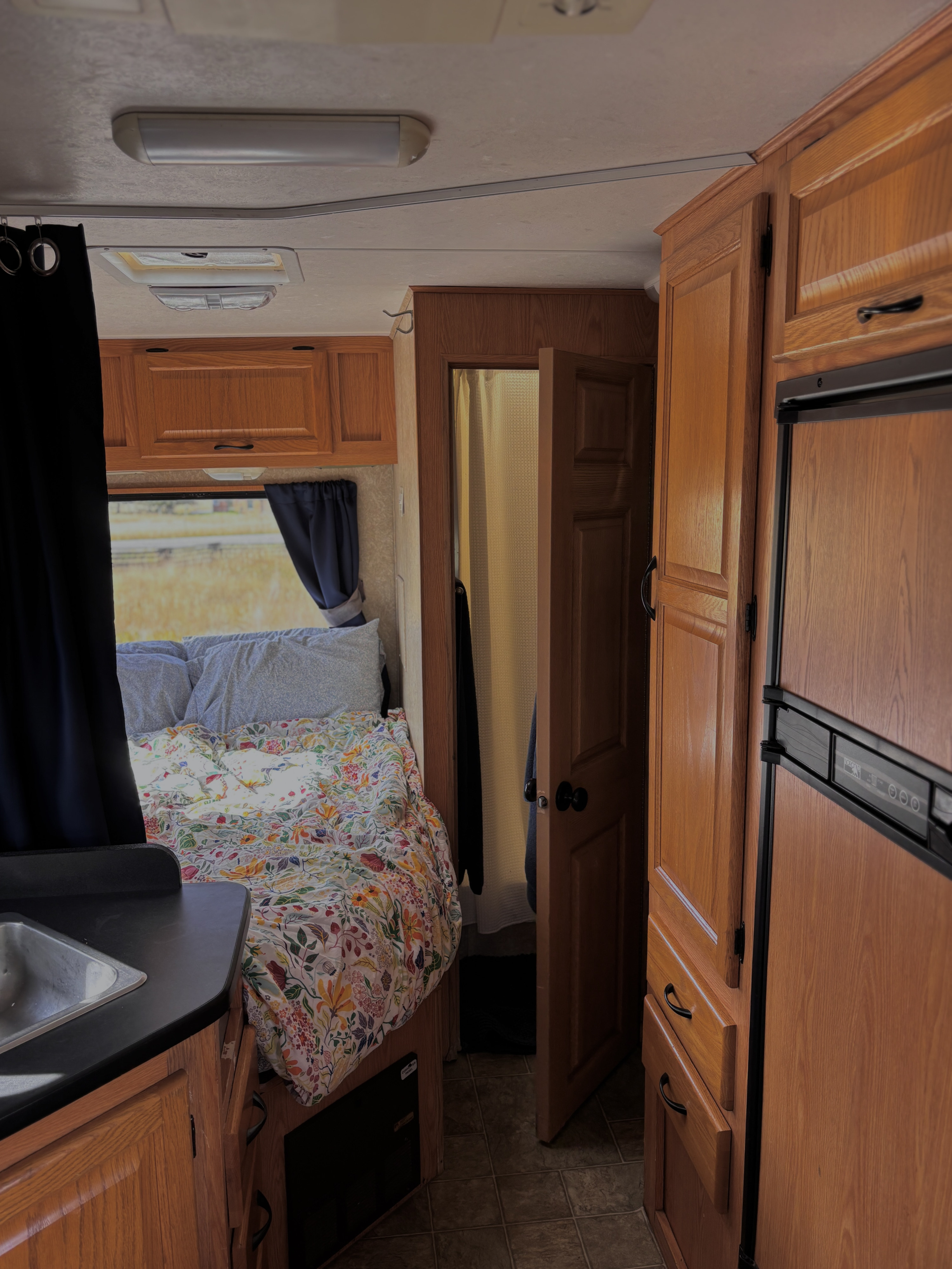 Cozy RV rental interior featuring a comfortable bed, compact kitchen sink area, and accessible bathroom, ideal for travel.. Four Winds Majestic 2006