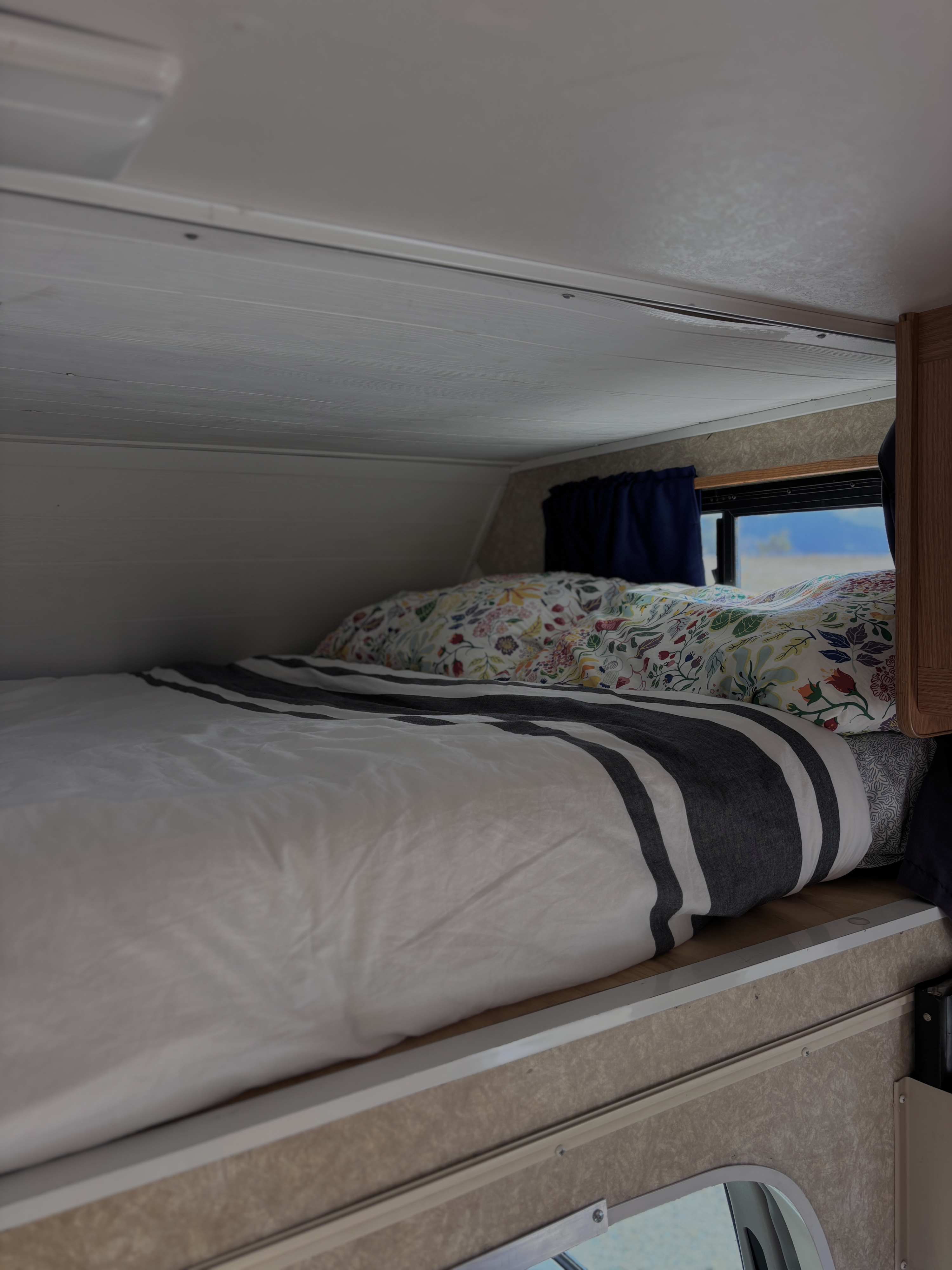RV rental's cozy sleeping area: a striped duvet, floral pillow, and window view offer a comfortable camper bed.. Four Winds Majestic 2006