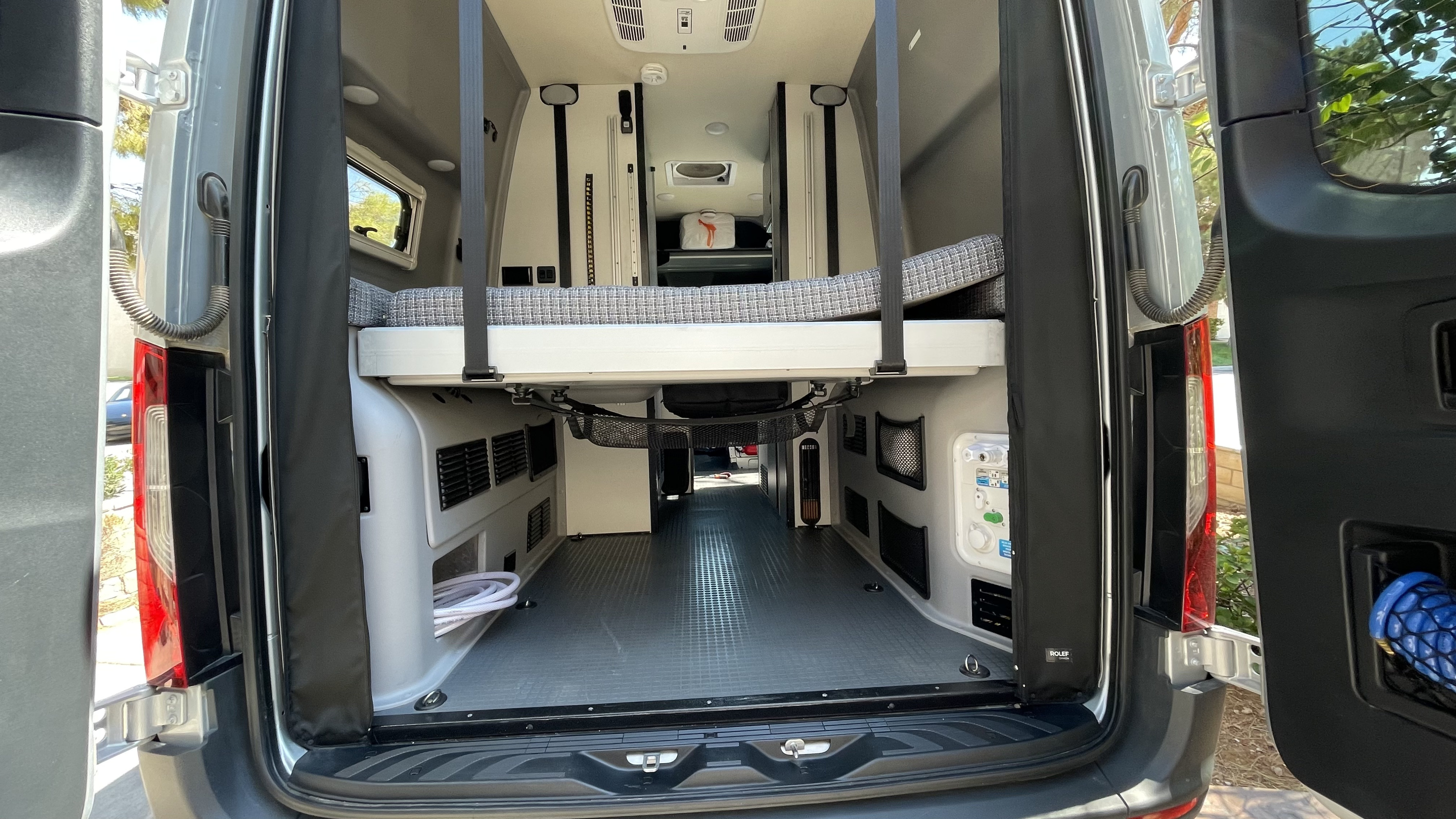 Inside an RV rental, a raised bed sits above a spacious cargo area with utility connections, perfect for your next trip.. Winnebago Revel 2021