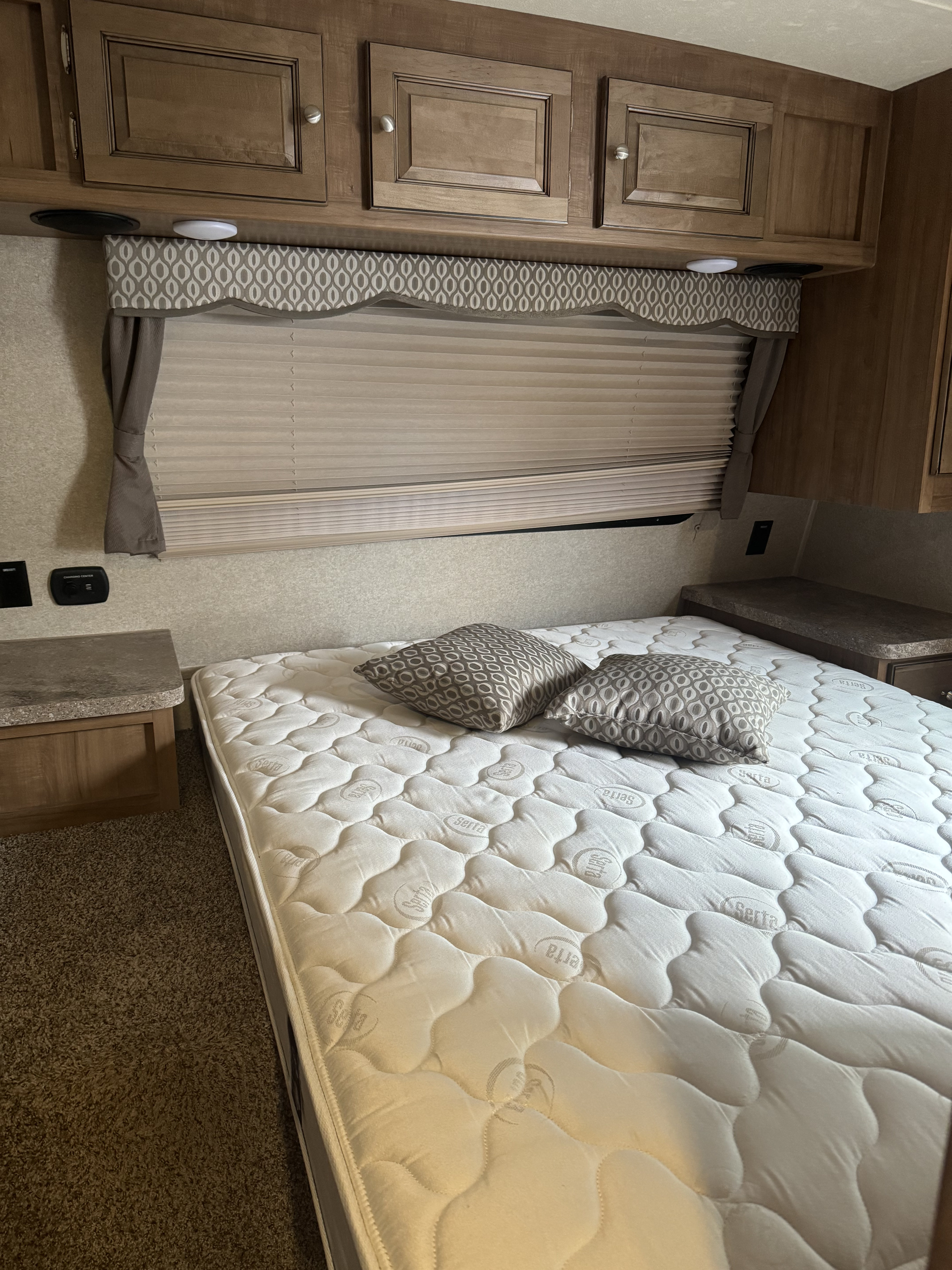 Inside an RV rental: a comfortable Serta mattress, patterned pillows, wooden cabinets, and window blinds.. Forest River Flagstaff Super Lite 2017