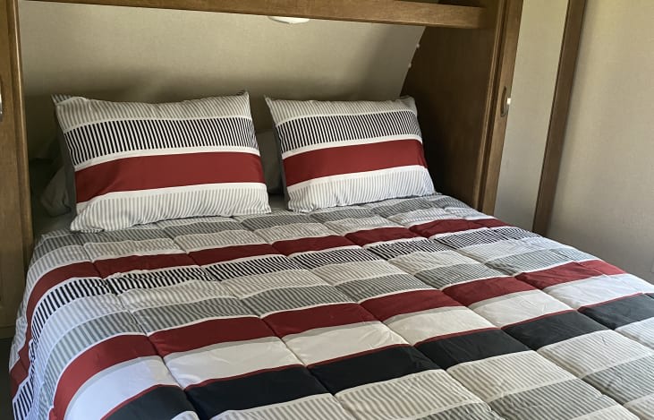Cozy RV rental bed with striped comforter and pillows in red, white, black, and gray.. Forest River Wildwood 2018