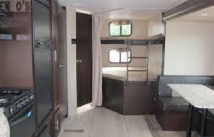 This RV interior, ideal for rv rental, features bunk beds, a compact kitchen with stove, and a cozy dinette area.. KZ Sportsmen LE 2018