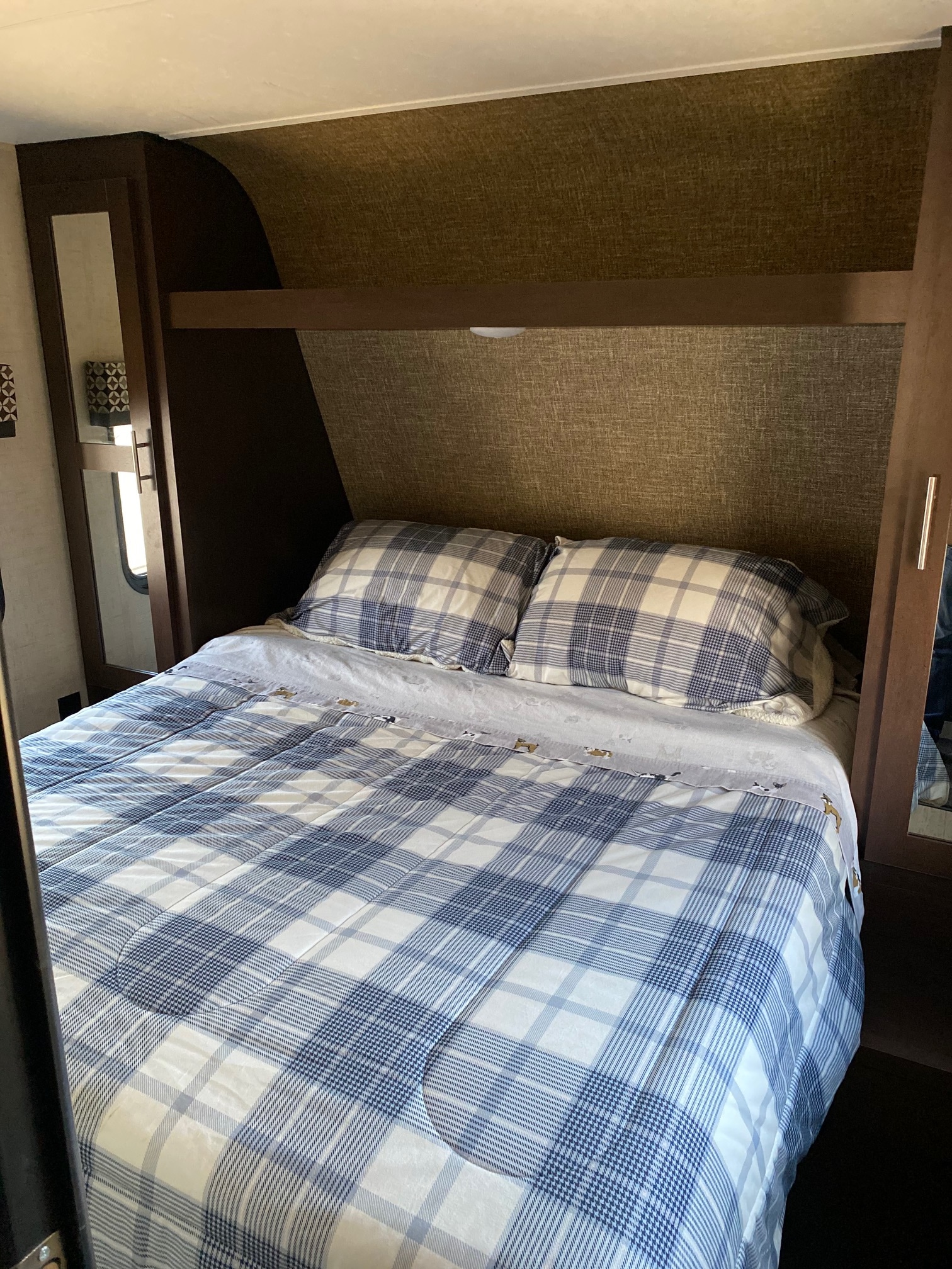 Cozy RV rental bedroom featuring a bed with blue plaid bedding, pillows, and built-in storage cabinets.. KZ Sportsmen LE 2018
