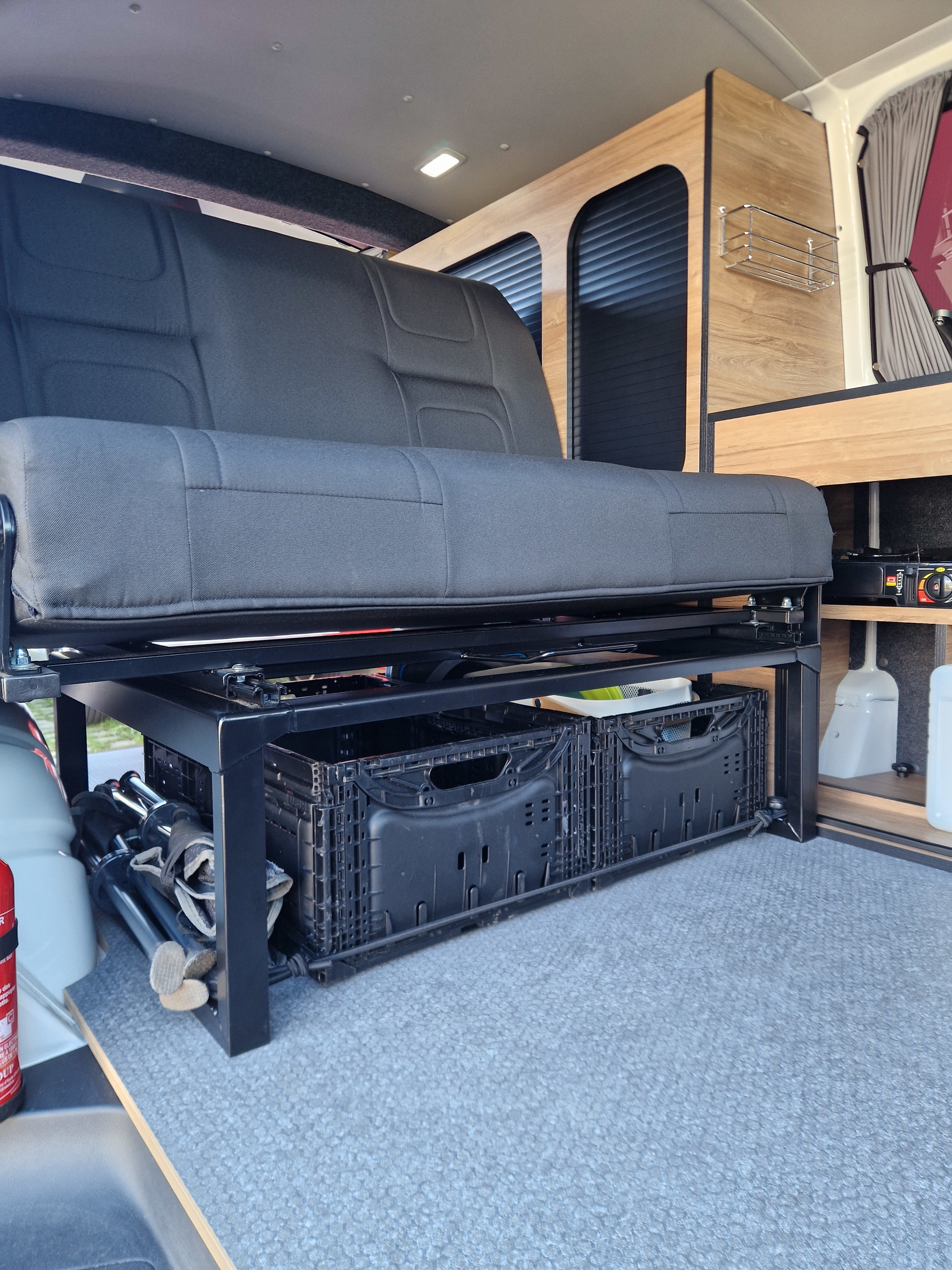 RV rental interior: Convertible bench seat, under-seat storage crates, and built-in cabinetry with a stove and lights.. Volkswagen Transporter T6 2025
