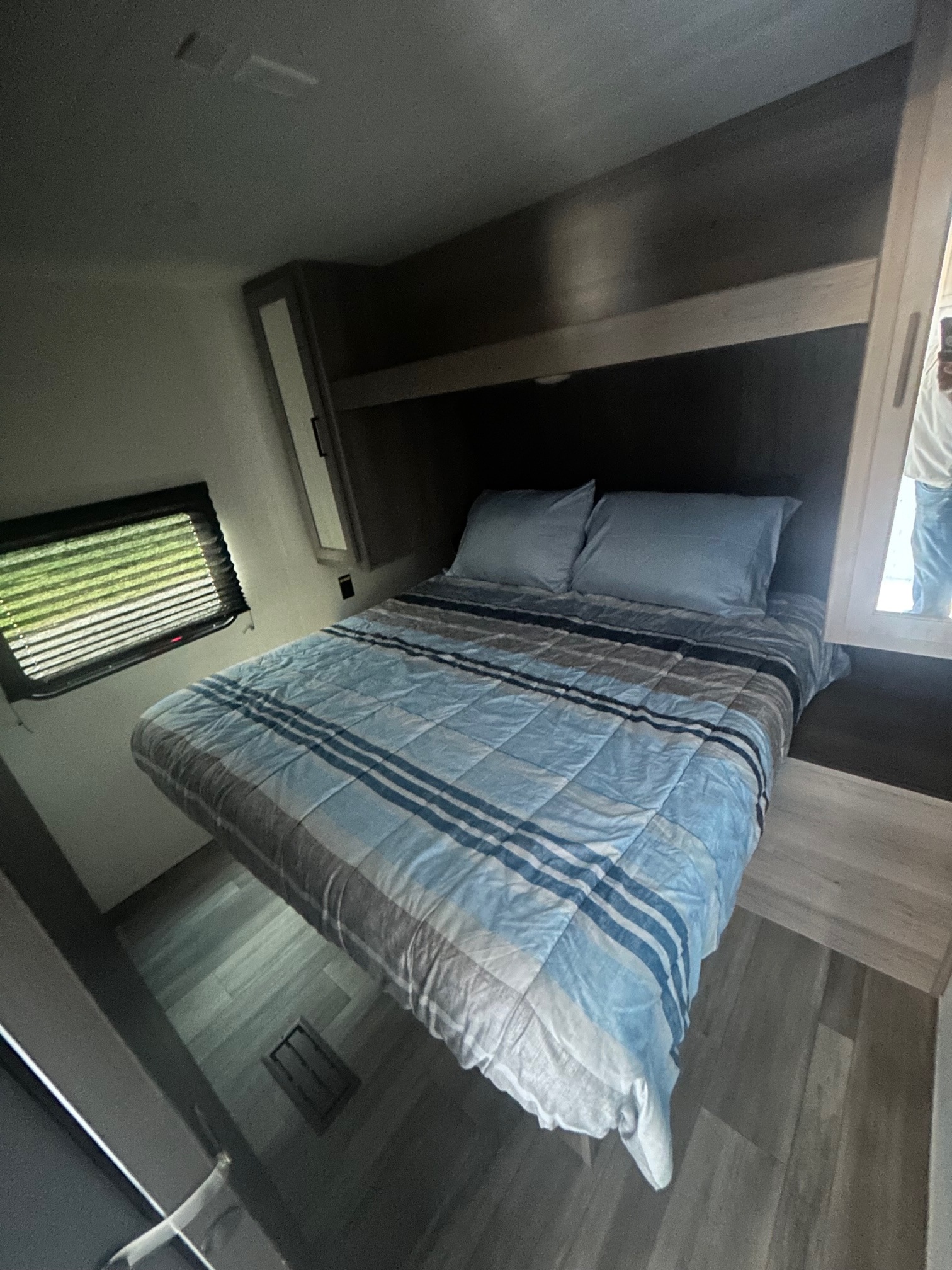 RV rental bedroom: a comfy bed with blue striped bedding, window, wood-look floor, and built-in storage.. Keystone RV Hideout Sport 2024