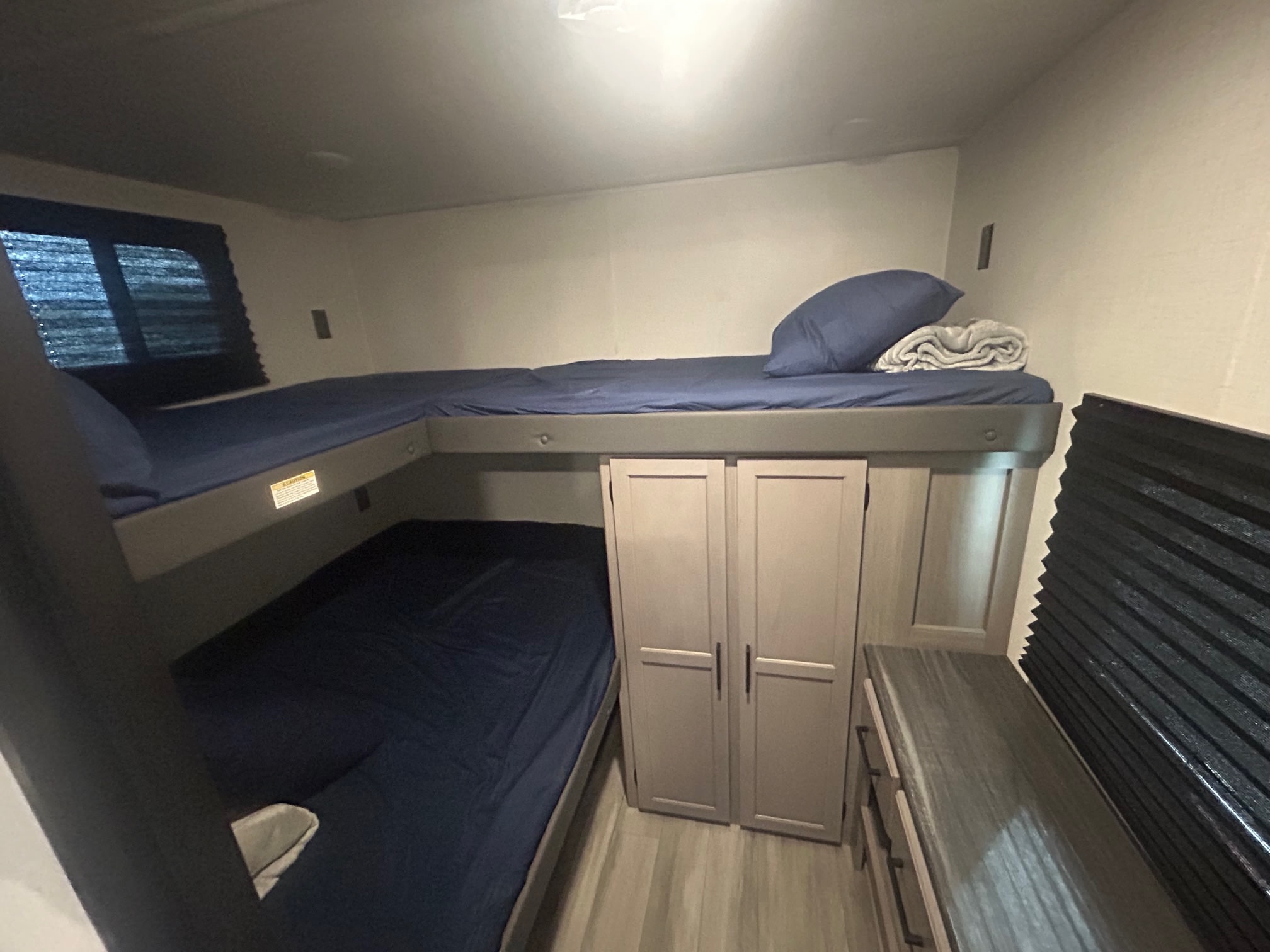 Interior of an RV rental: bunk beds with blue bedding, a small closet, and a dresser provide sleeping for your adventure.. Keystone RV Hideout Sport 2024
