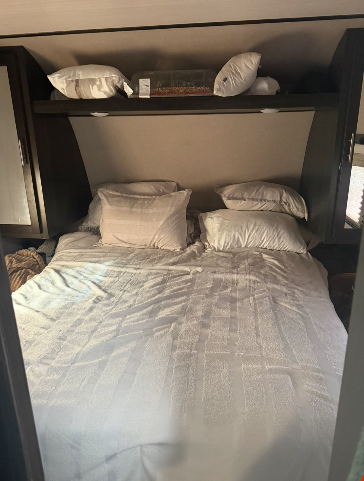 An RV rental bedroom with a white, textured bedspread, numerous pillows, and an overhead shelf with stored items.. Forest River Nitro Xlr 2019