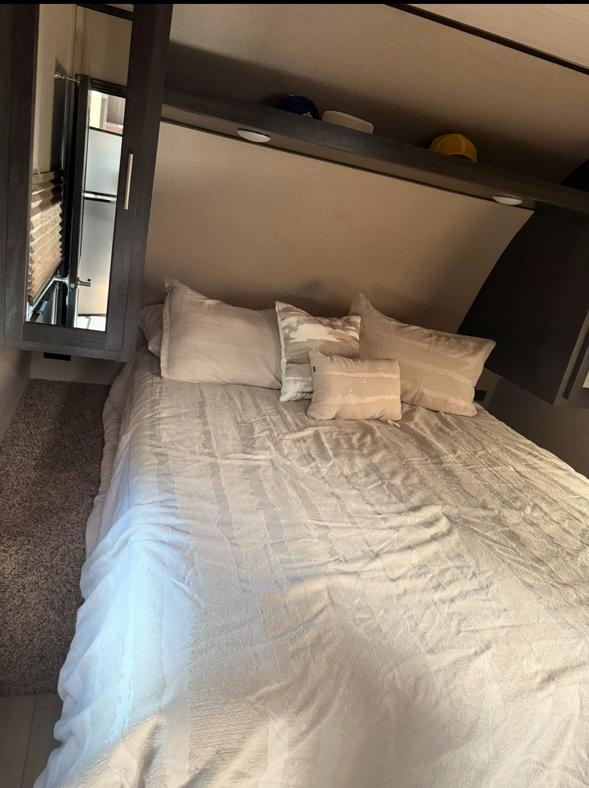 Cozy RV rental bedroom featuring a neatly made bed with light-colored bedding and pillows, overhead storage, and a mirror.. Forest River Nitro Xlr 2019