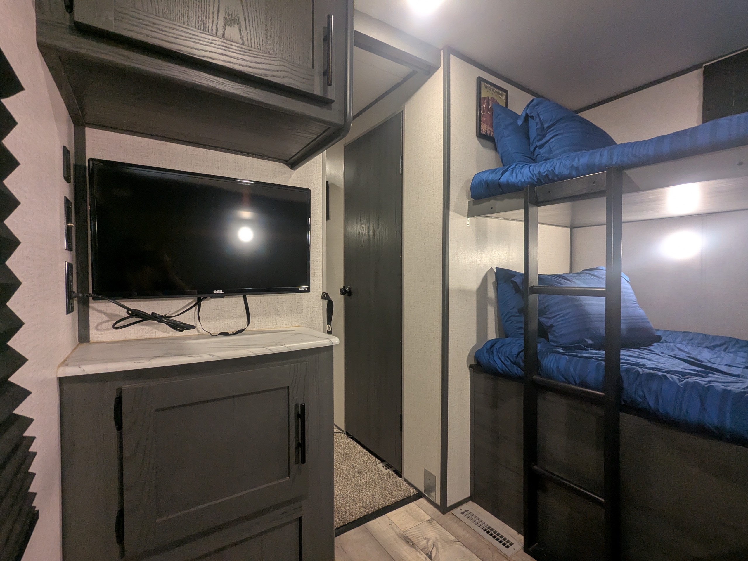 Cozy RV rental bunk area features blue-sheeted beds, a TV, and dark gray storage cabinets for a functional space.. Aspen Trail Aspen Trail Trailer 2021
