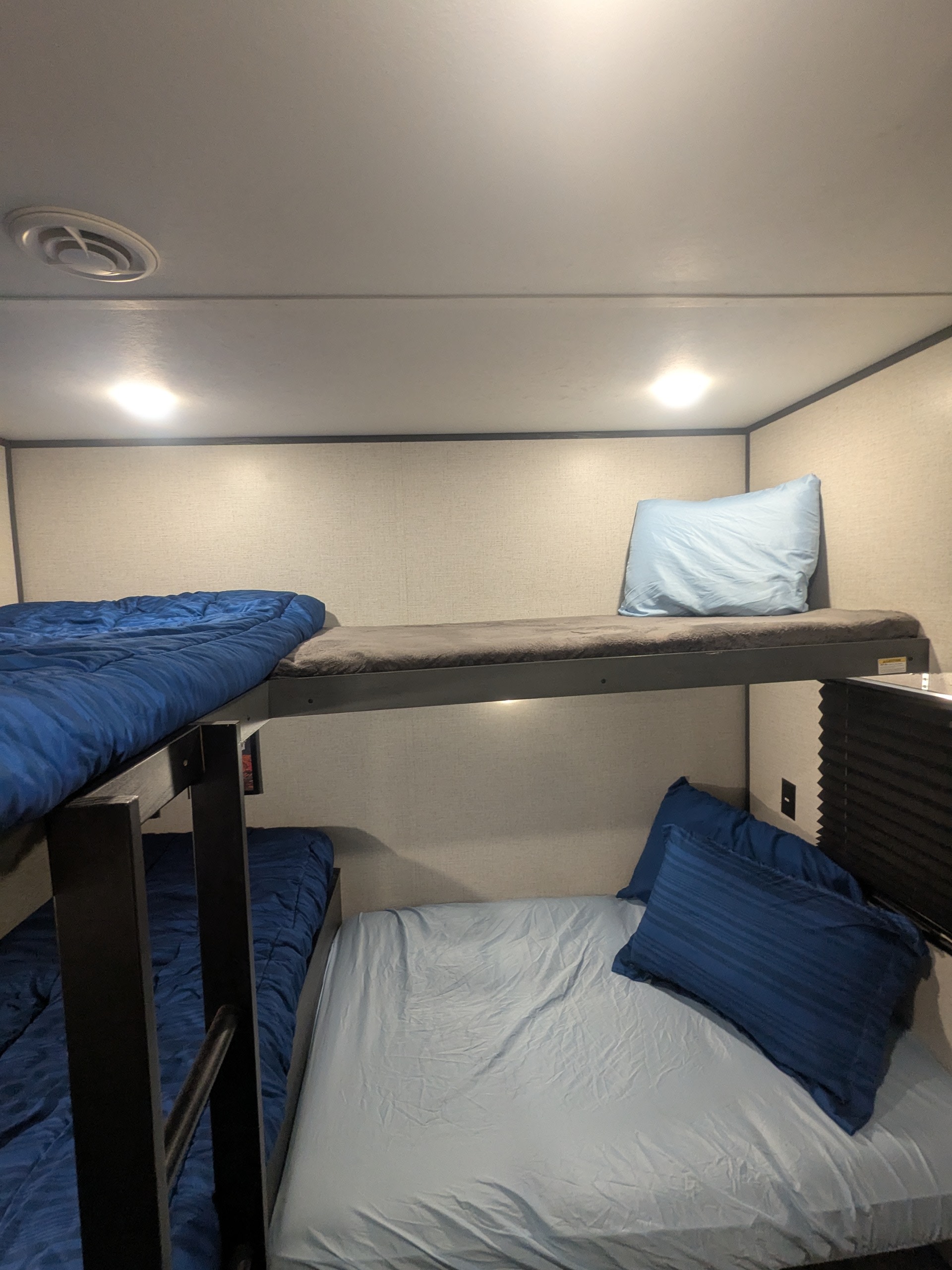 Cozy RV rental bunk beds with blue blankets and pillows, featuring overhead lighting and an air vent for a comfortable stay.. Aspen Trail Aspen Trail Trailer 2021