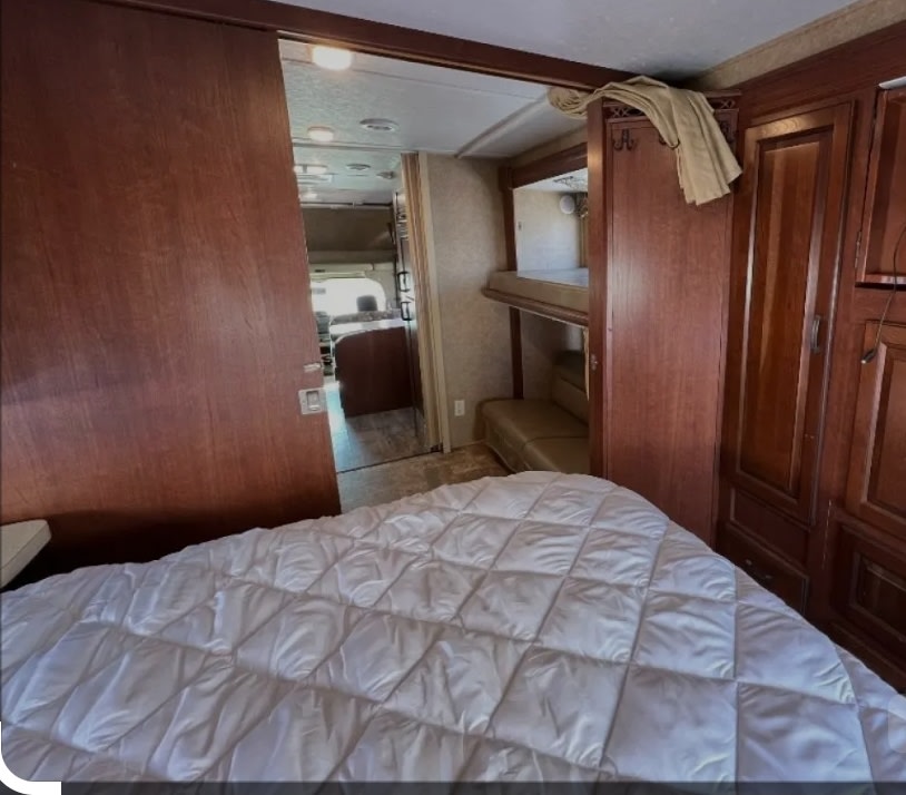 RV rental bedroom featuring a comfy bed, bunk beds, and a glimpse of the connecting living area through the sliding door.. Forest River Sunseeker 2015