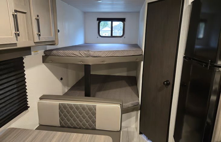 This RV rental interior features comfortable bunk beds, a dinette seating area, and a compact kitchen fridge, ideal for travelers.. Keystone RV Hideout Sport 2025