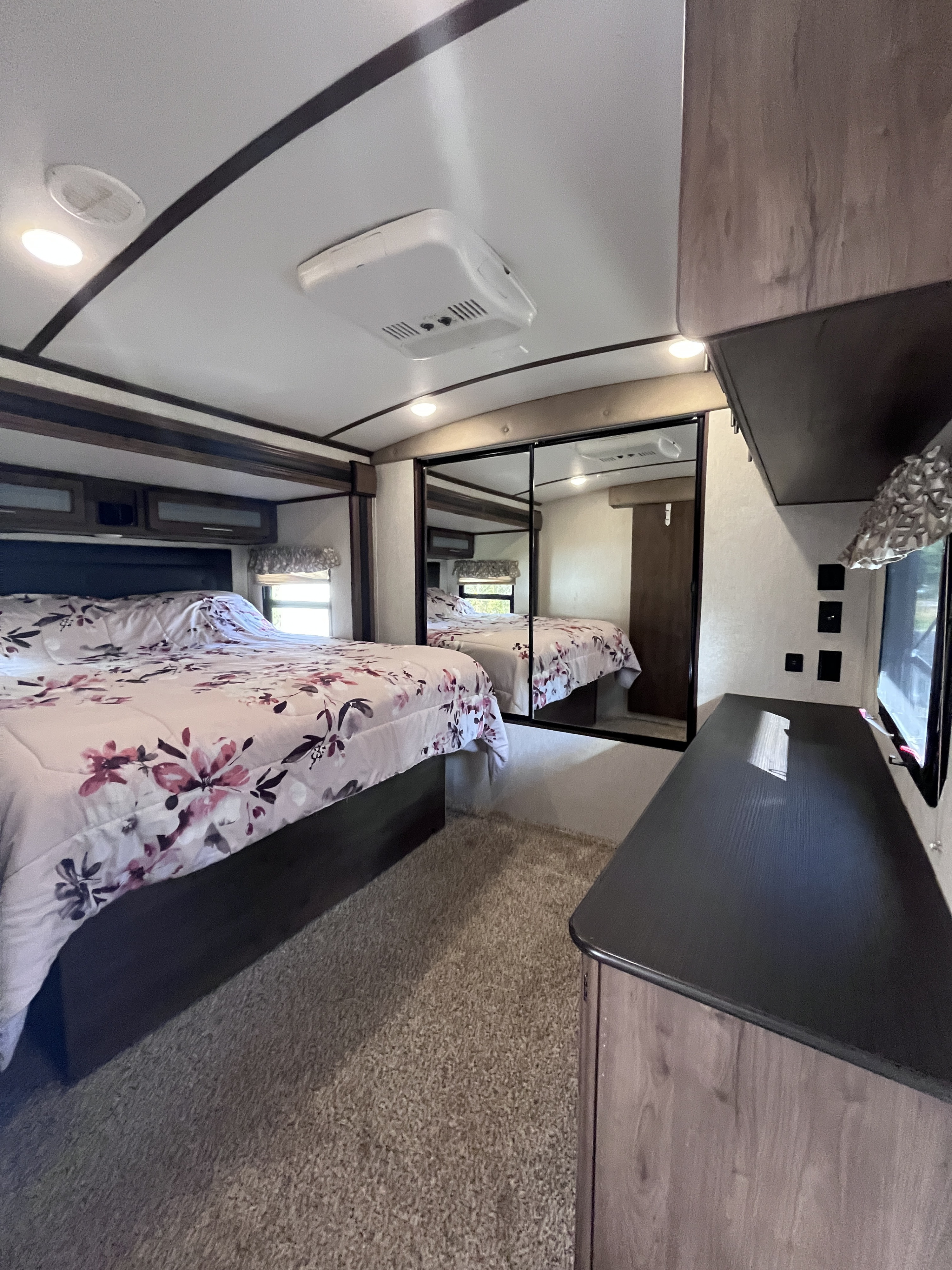 Relax in this comfortable RV rental bedroom with floral bedding, mirrored closet, TV, and ceiling AC.. Keystone RV Cougar X-Lite 2018