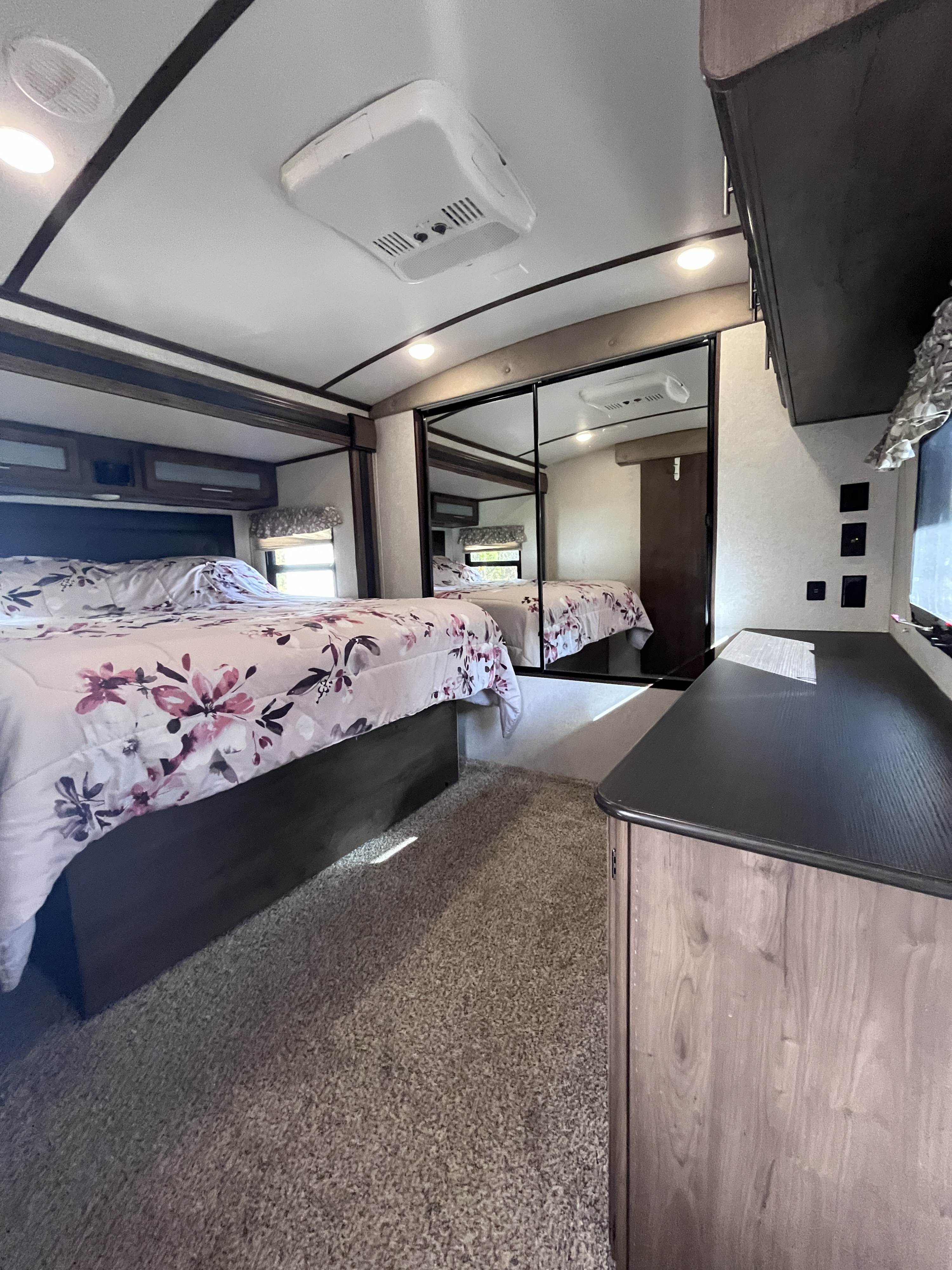 Cozy RV rental bedroom with a light floral comforter, mirrored closet, ceiling AC, and carpeted floor. Ideal for travels.. Keystone RV Cougar X-Lite 2018