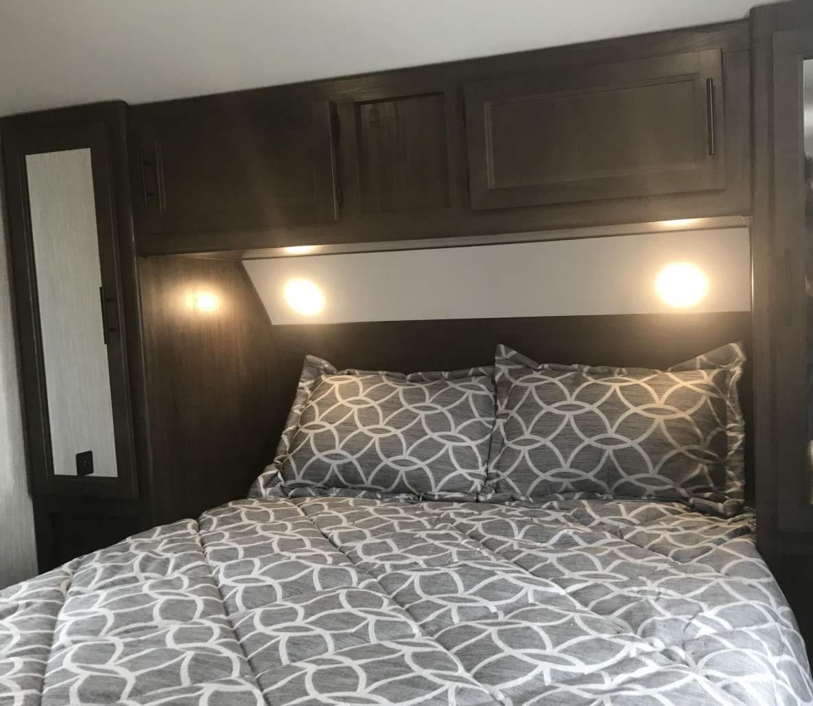 Cozy RV rental bedroom featuring patterned bedding, dark wood cabinetry, and bright reading lights. Perfect for your next adventure.. Forest River Cherokee 2021