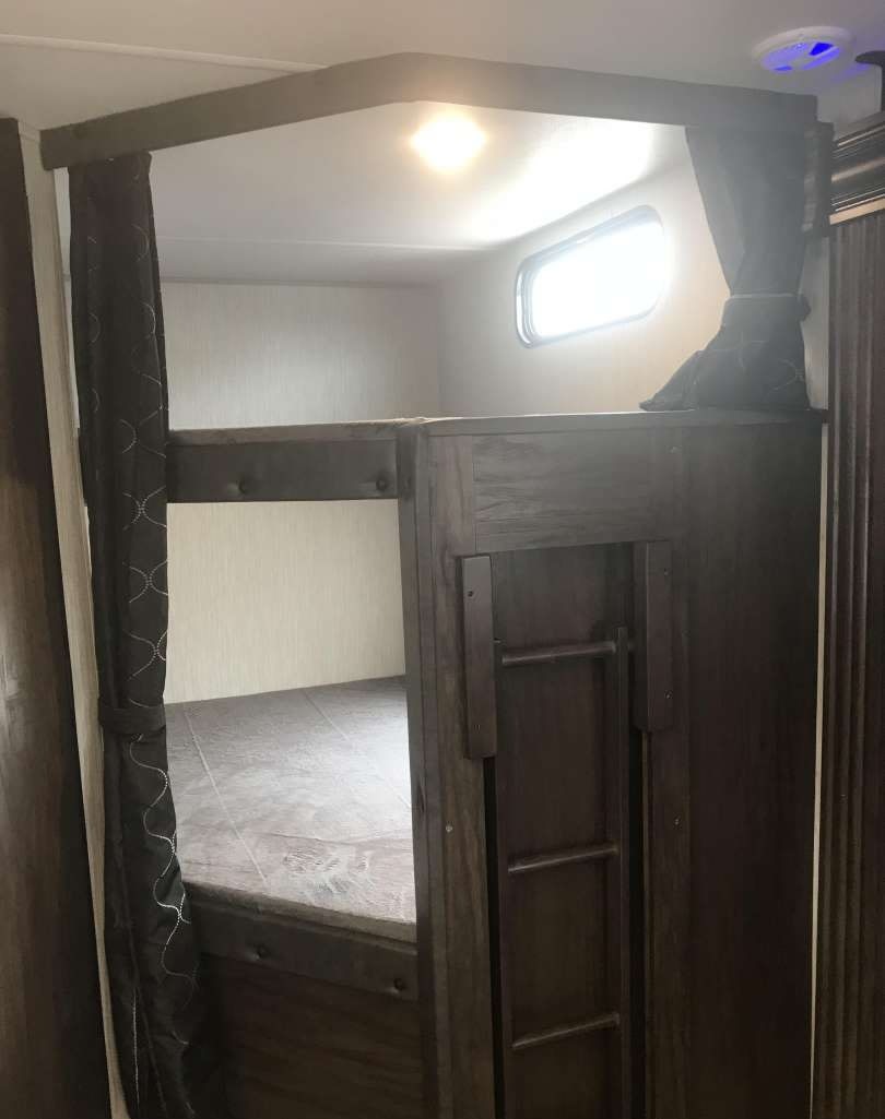 This RV rental interior features cozy bunk beds with privacy curtains, a small window, and an attached ladder.. Forest River Cherokee 2021