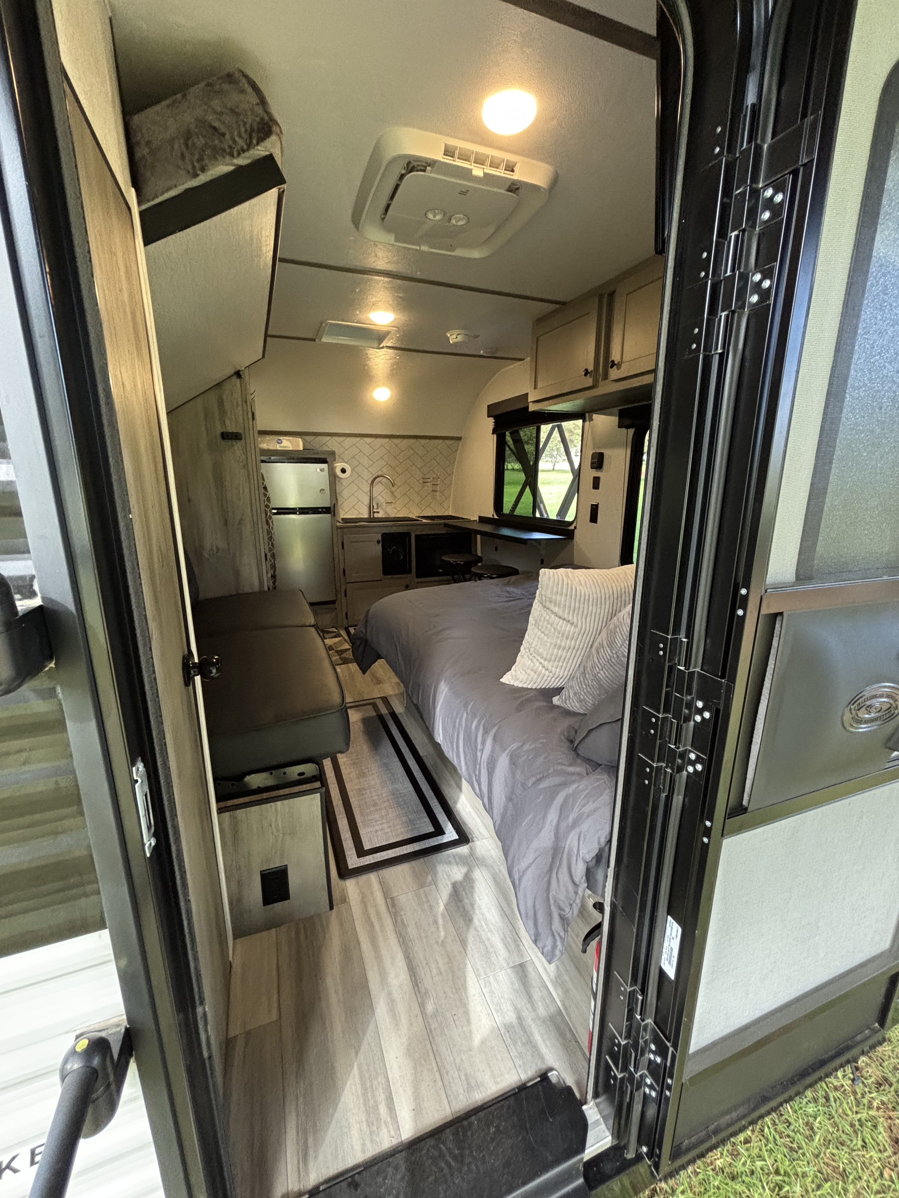 View into a compact RV rental camper, showing a cozy bed, kitchenette, dinette, and ceiling AC unit.. Go Lite Wayfinder 2026