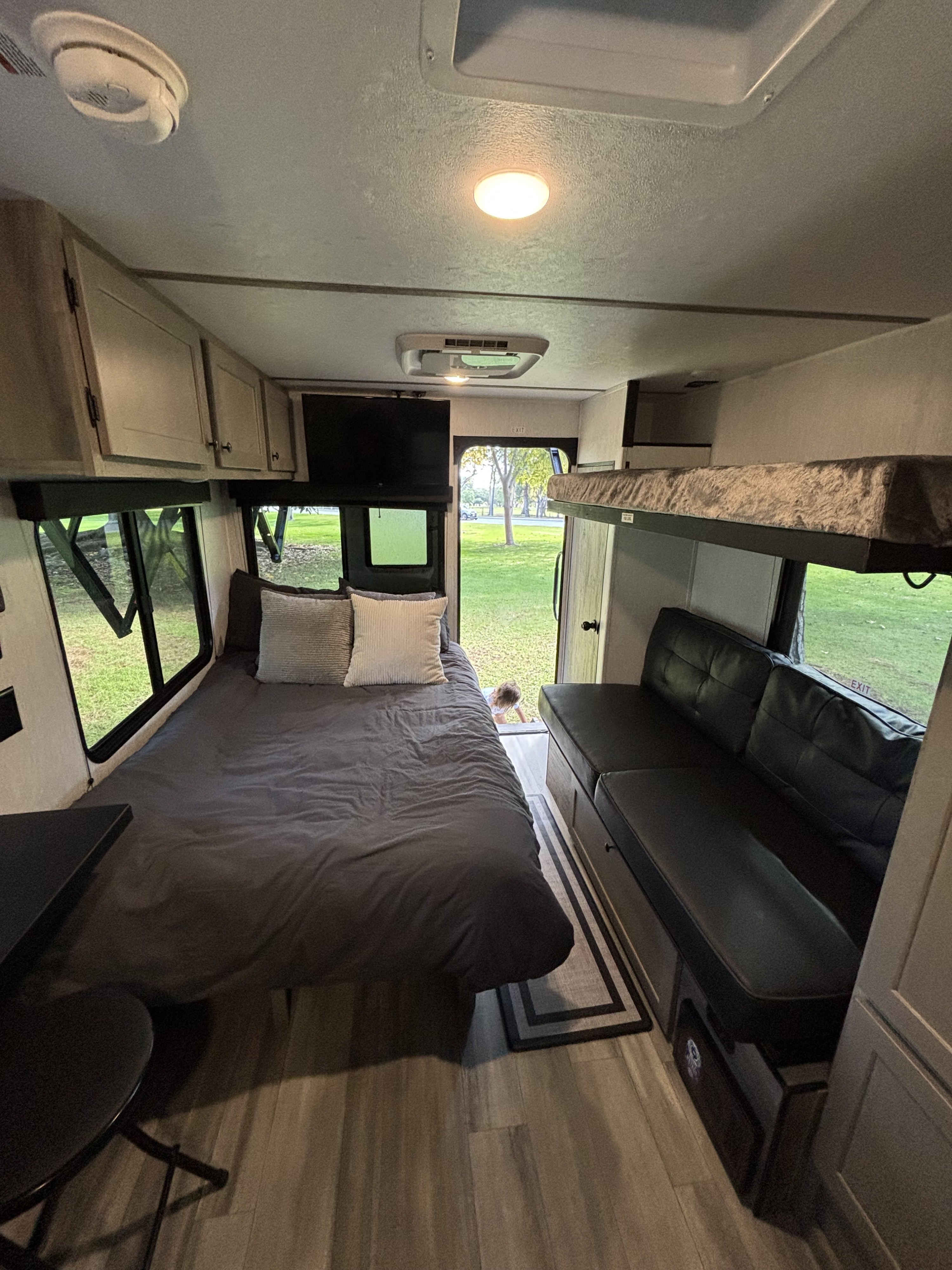 Cozy RV rental interior with bed, bunk beds, sofa, and TV. Features windows overlooking green outdoors and a child peeking.. Go Lite Wayfinder 2026