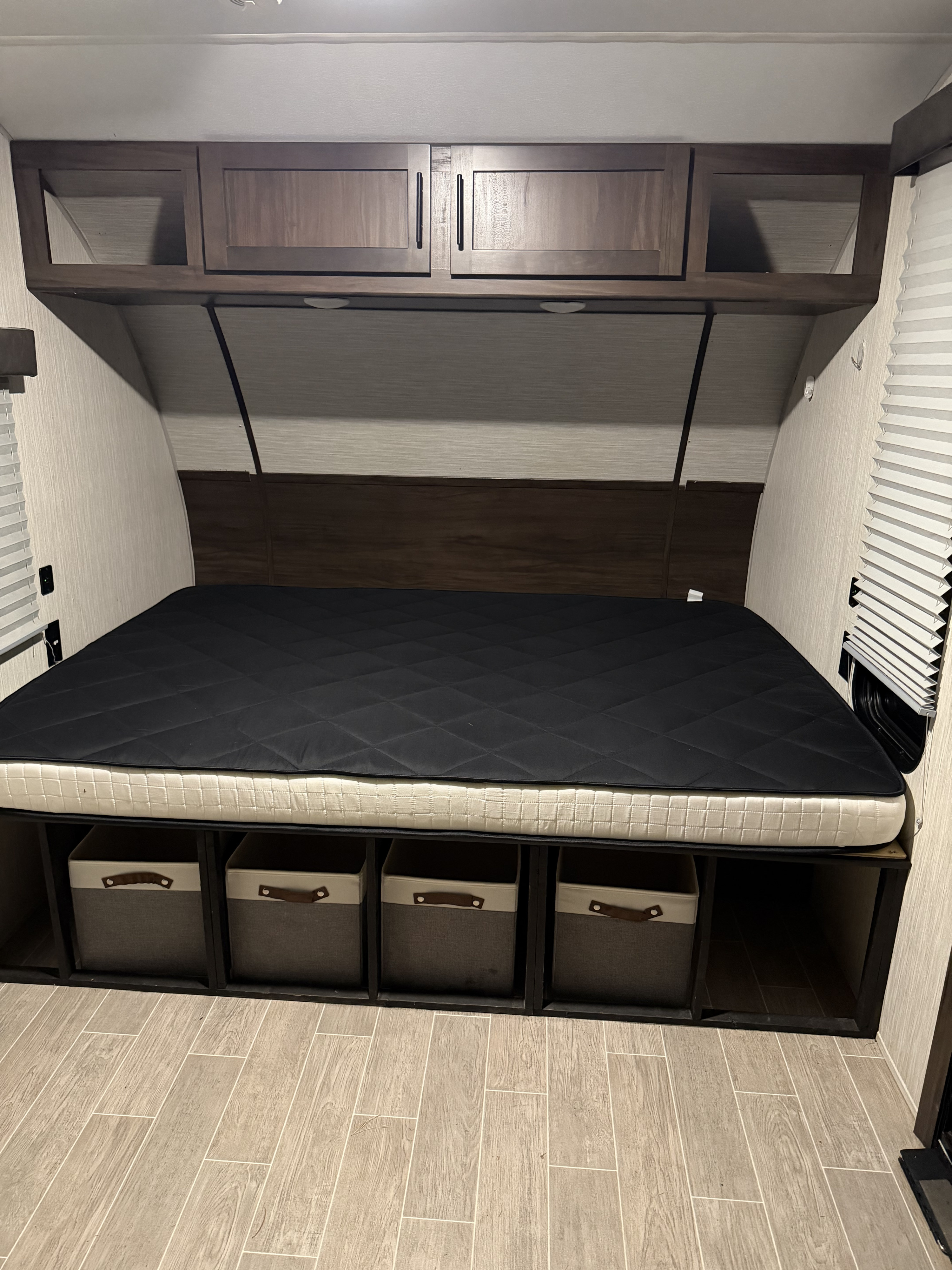 RV rental bedroom featuring a bed with a dark mattress topper, overhead cabinets, and under-bed storage.. Forest River Cherokee Wolf Pup 2021