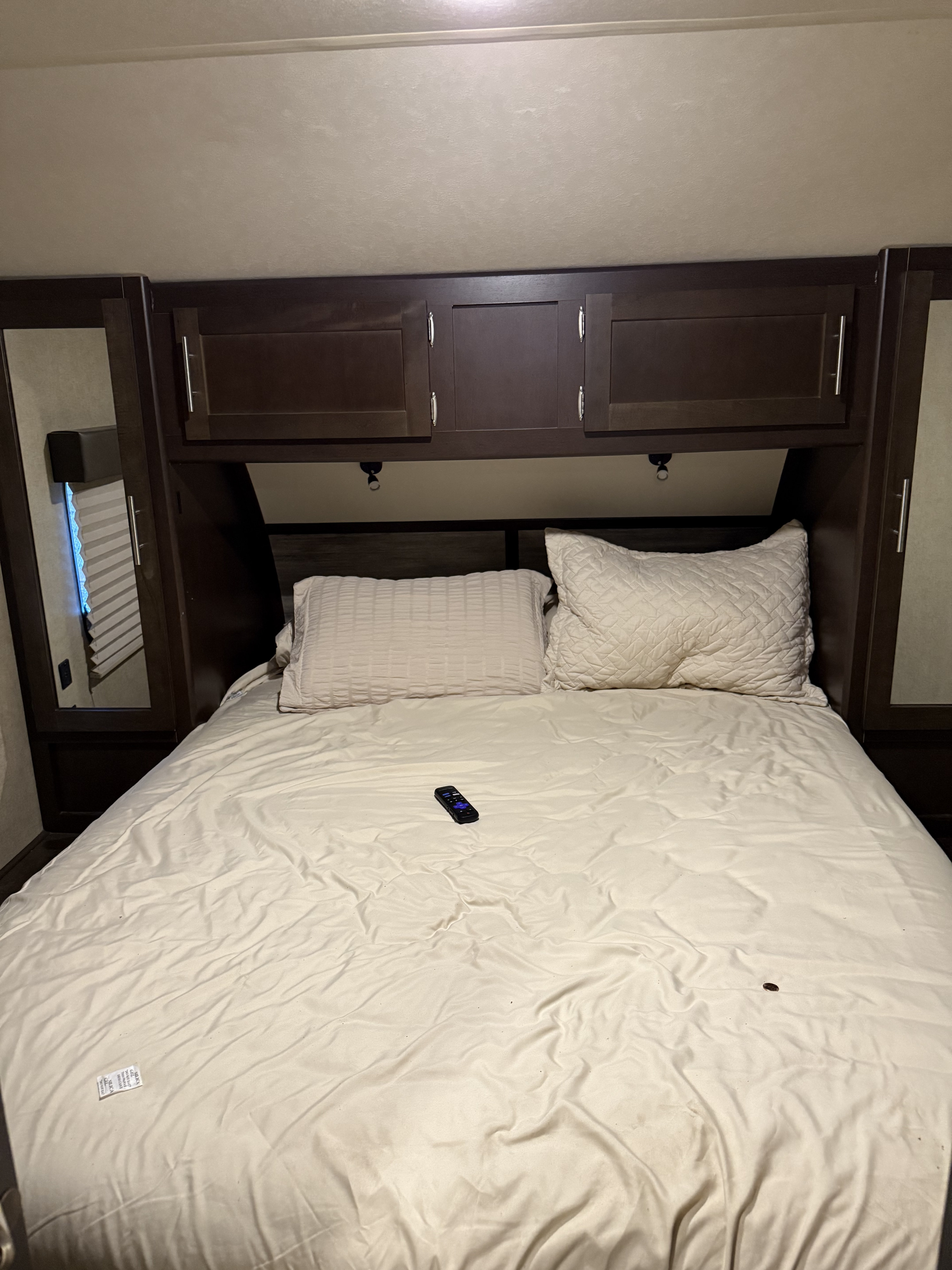 RV rental bedroom shows a bed with light bedding, dark wood cabinetry, and a remote resting on the sheets.. Forest River Cherokee 2016