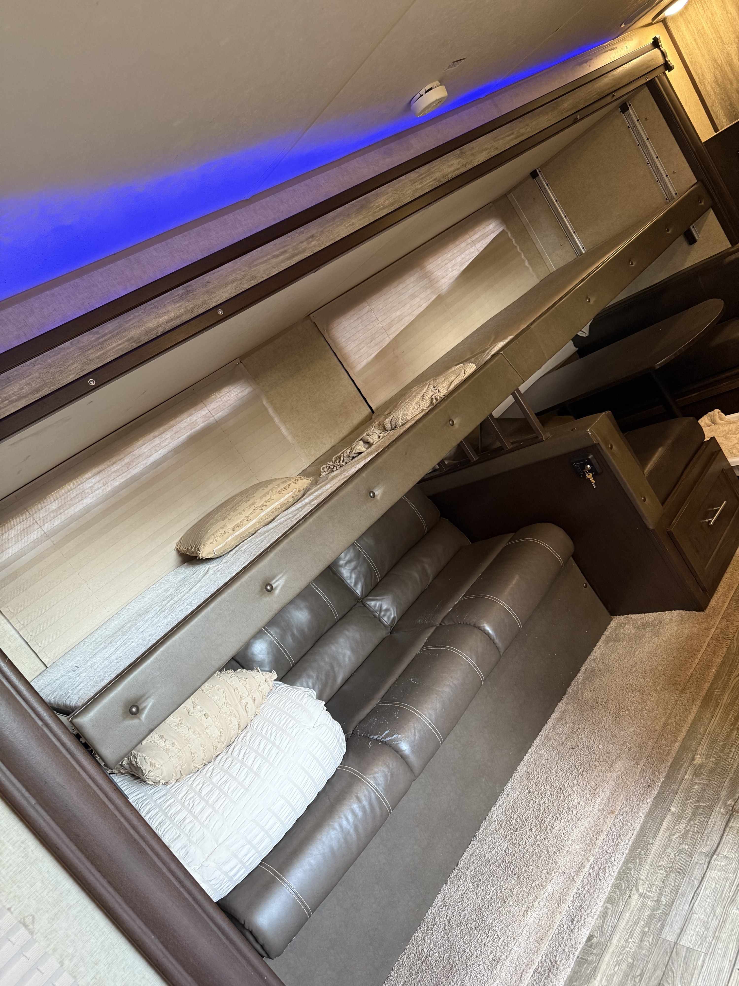 Inside this RV rental, see a cozy sofa, an overhead fold-down bed, and blue accent lighting, perfect for comfortable travel.. Forest River Cherokee 2016