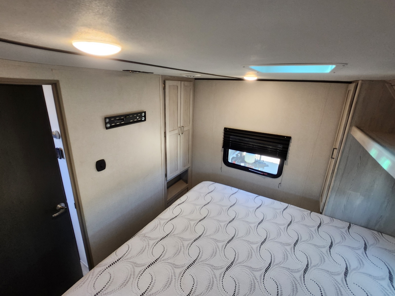 RV rental bedroom: a bright space with a comfy, patterned bed, window, wall-mounted panel, and wardrobe, ideal for your next trip.. Keystone RV Sprinter Limited 2021